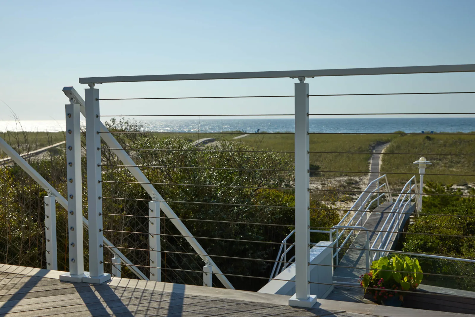 White cable railing on a deck overlooking dunes and the ocean beyond