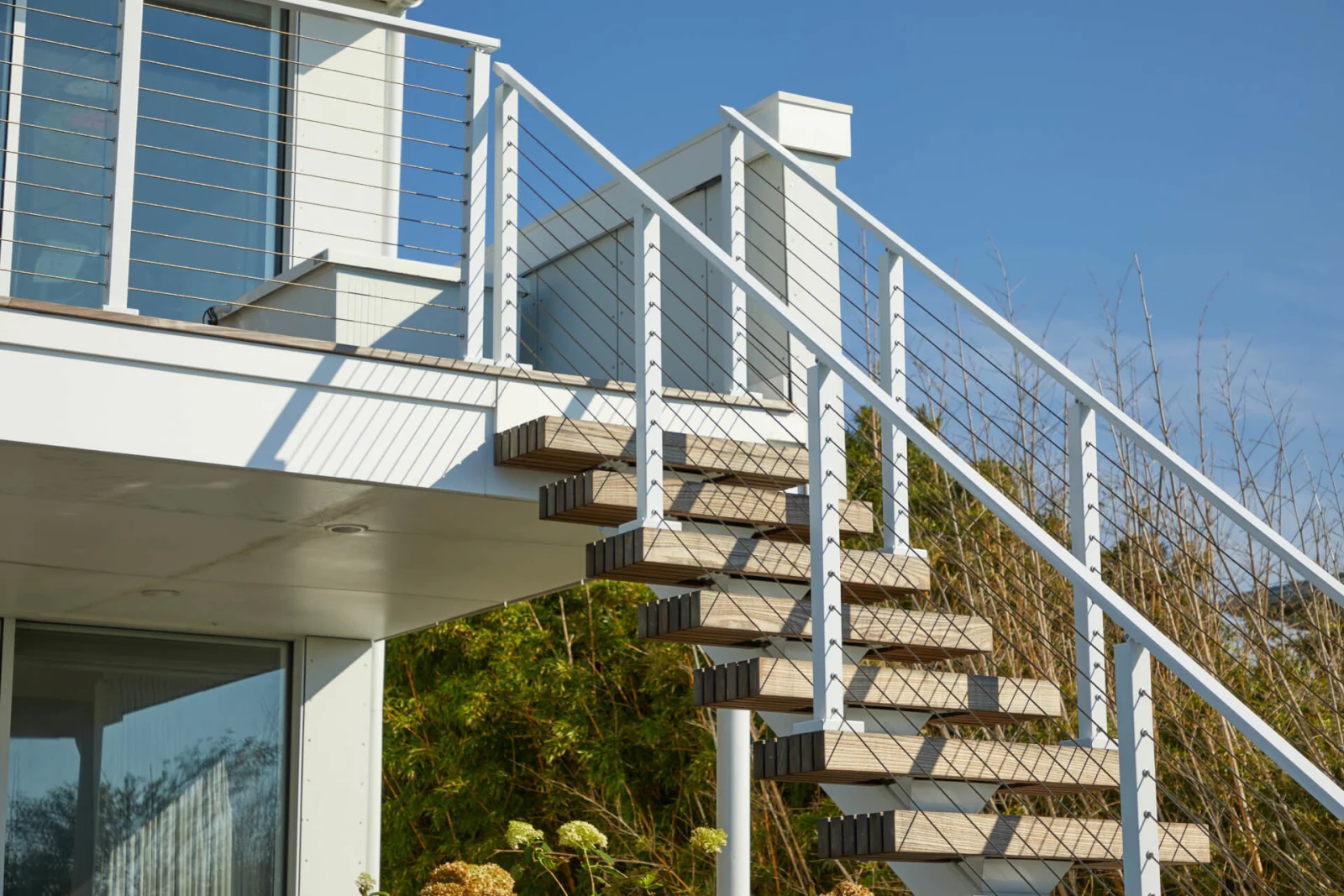 Outdoor flight rising to a raised deck with white posts and cable infill