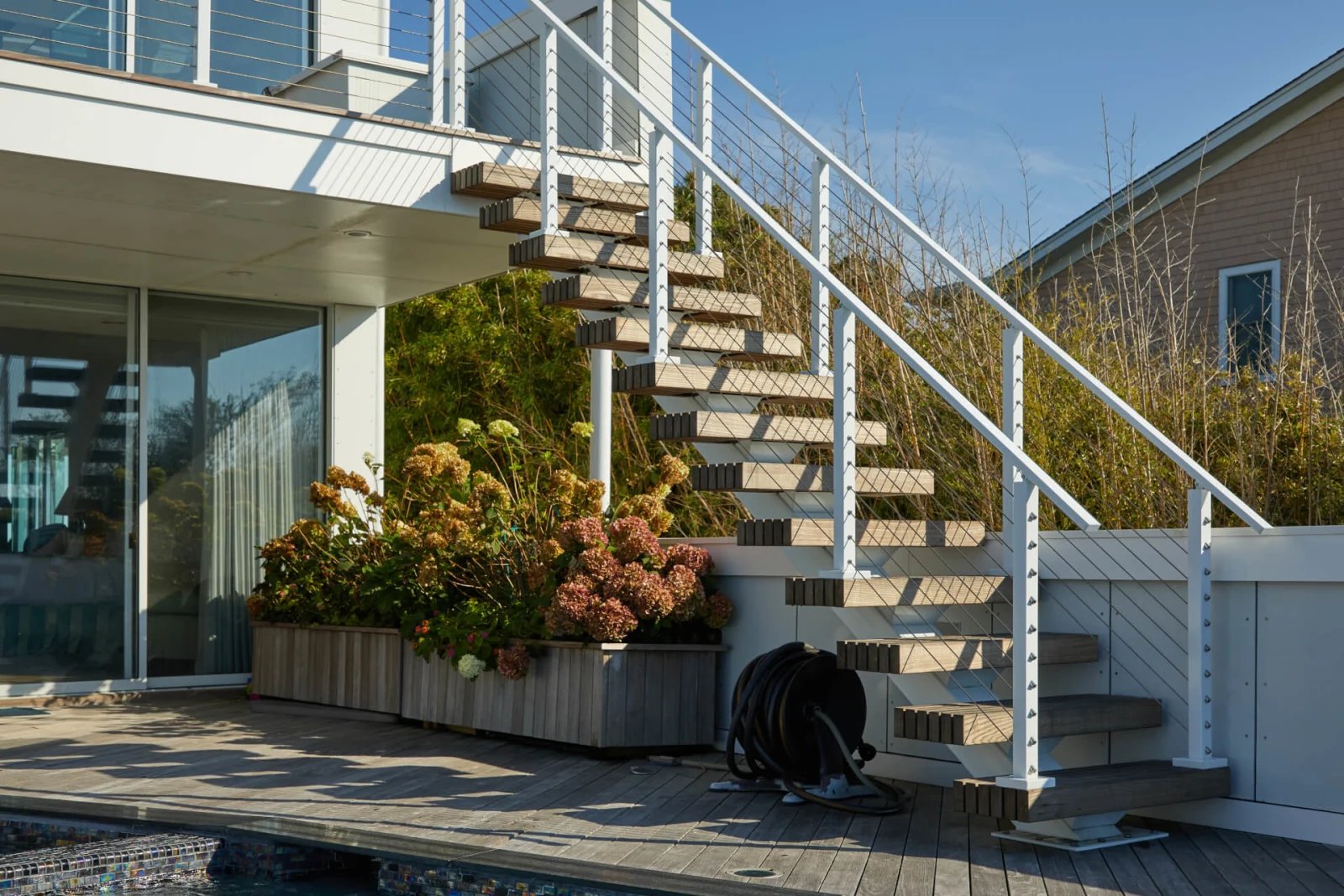 Outdoor stair beside deep planters with cable railing continuing along the deck