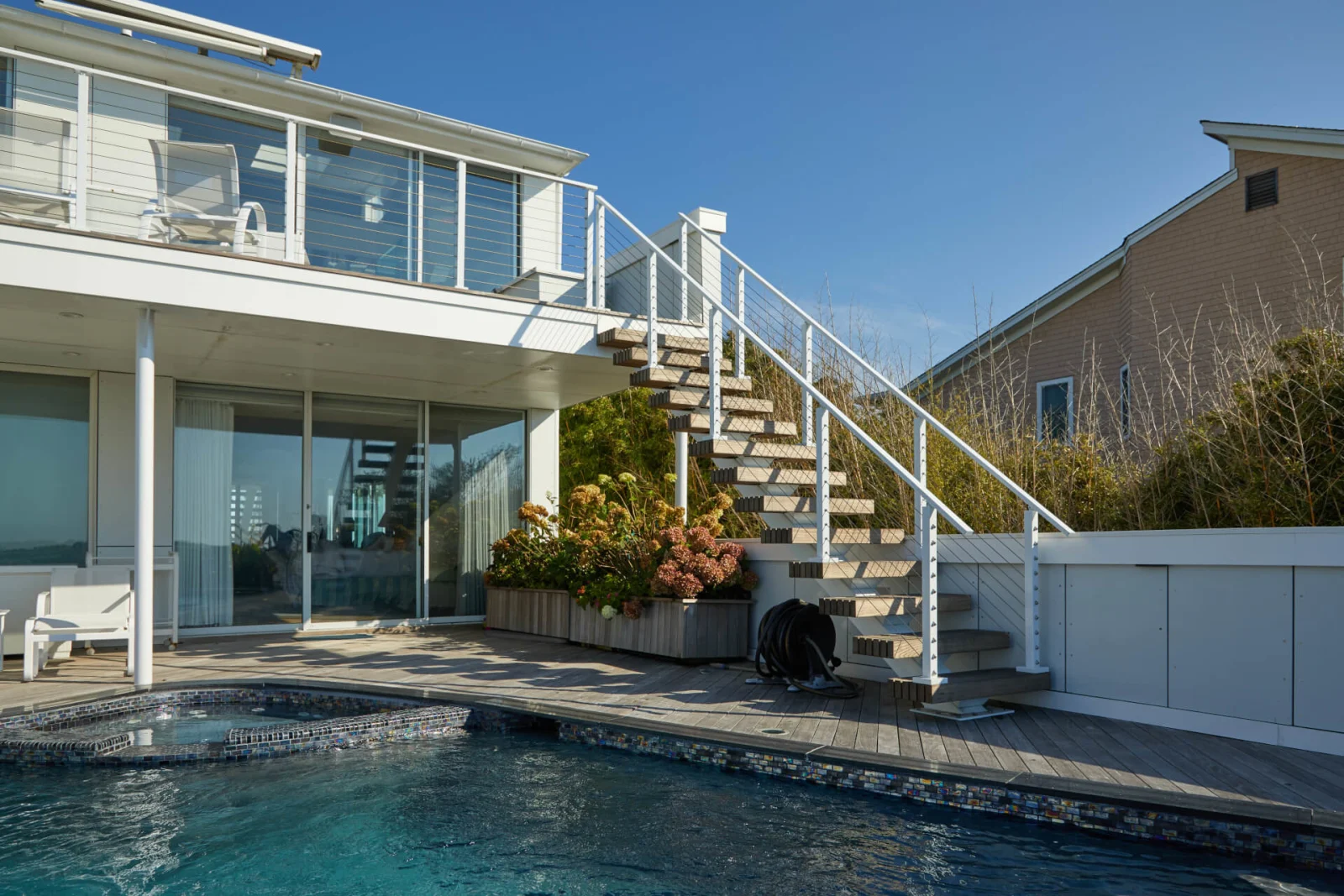 White outdoor stair with wood treads climbing from a pool deck to an upper balcony