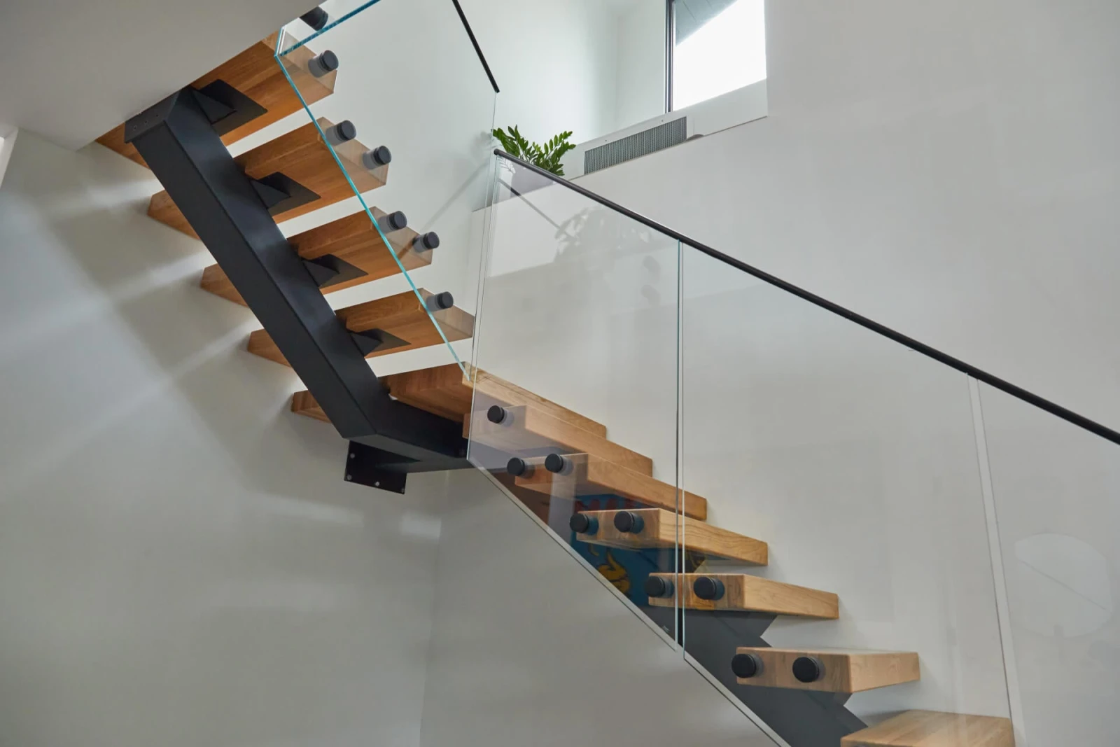 Stair turning below the balcony with pinned glass panels following the run