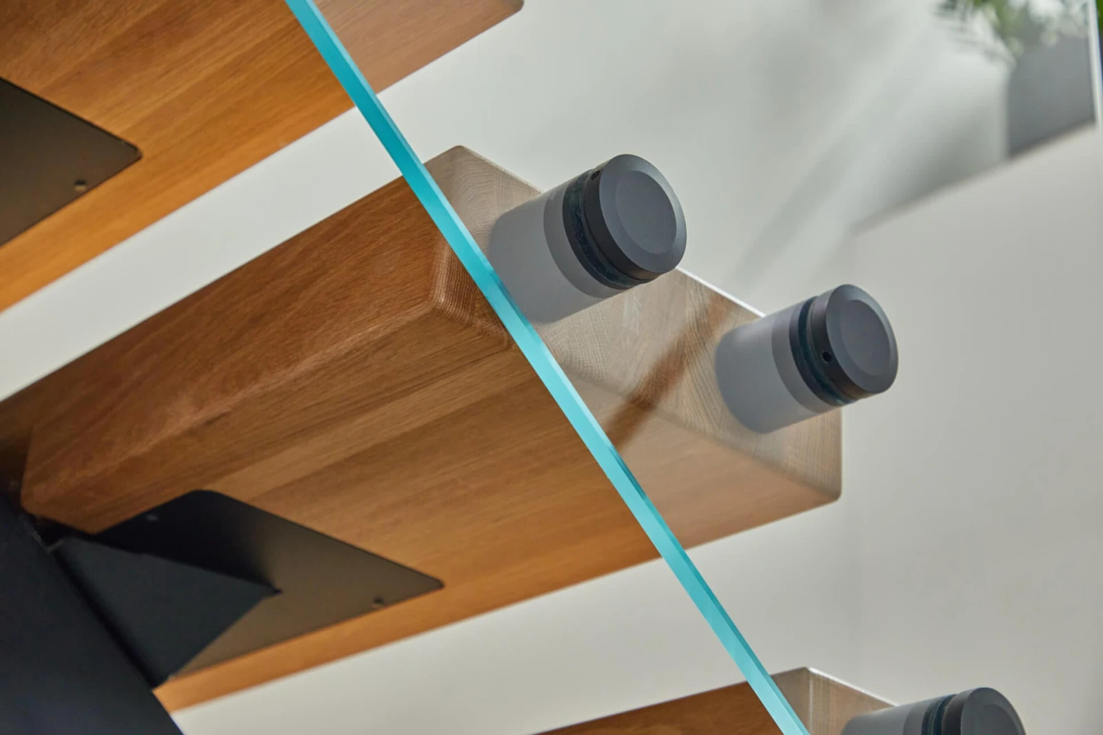 Close detail of black standoff pins clamping glass to a pale wood tread