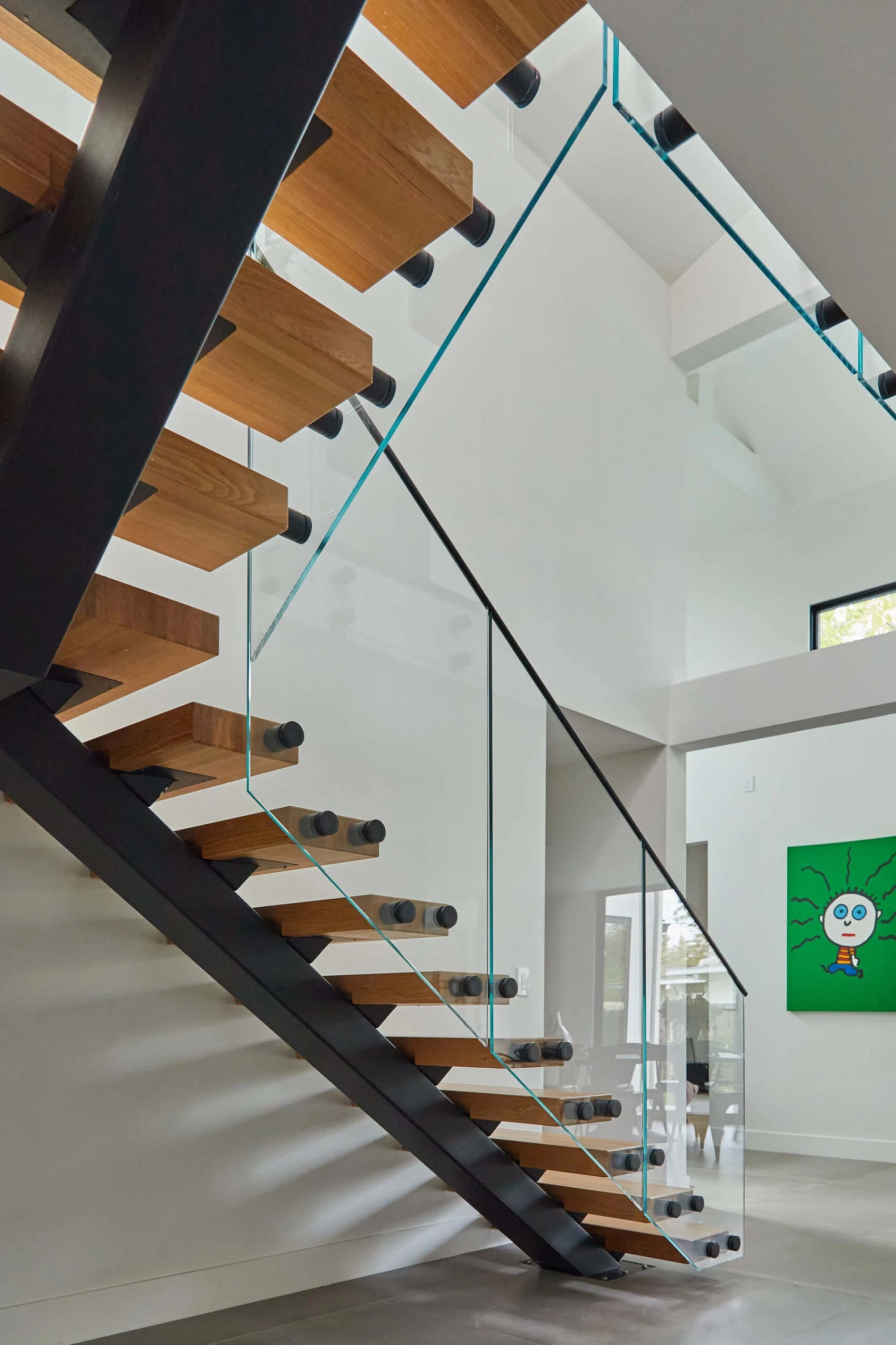 Pale treads on a black stringer with glass railing beneath a vaulted ceiling