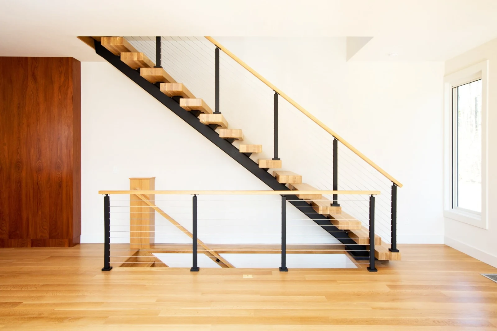 Straight-on view of a black stringer stair with cable railing in an empty bright room