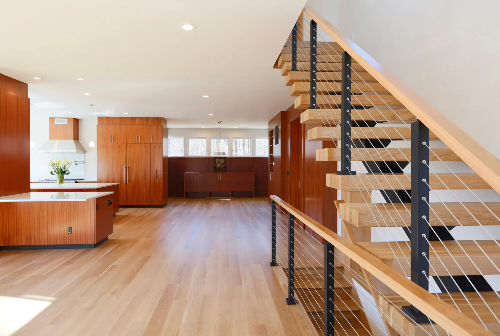 Kitchen and dining space with the open stair rising behind a cable railing