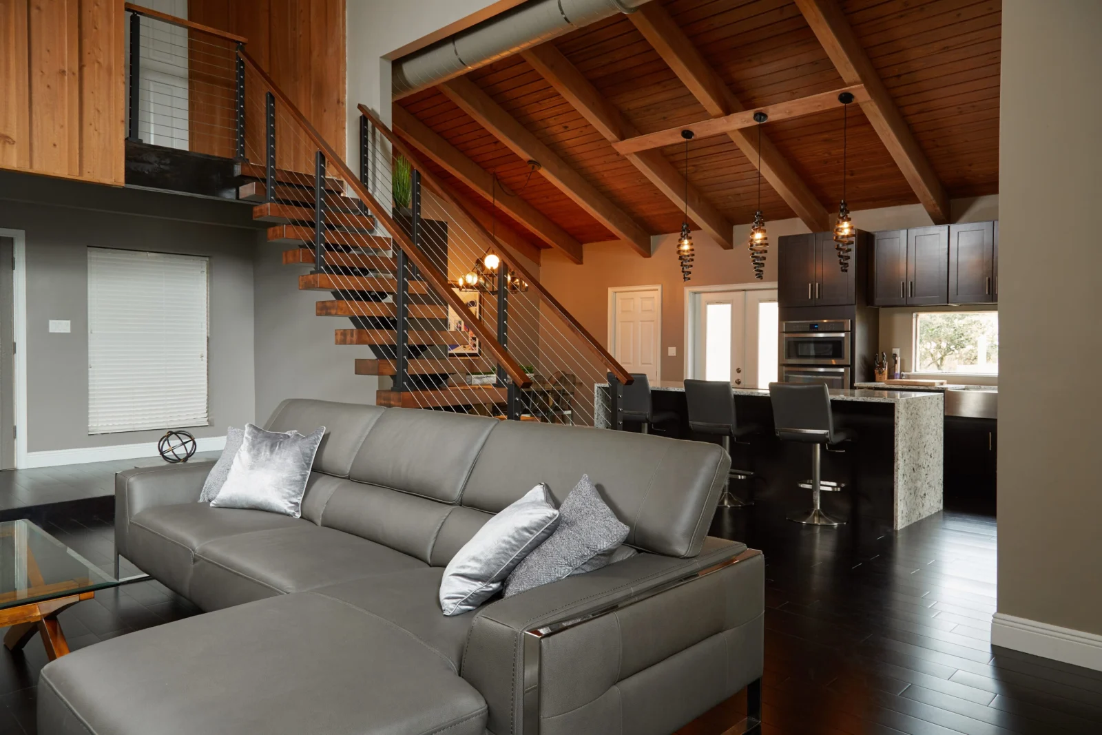 Living room with gray sectional below a beamed wood ceiling and open stair