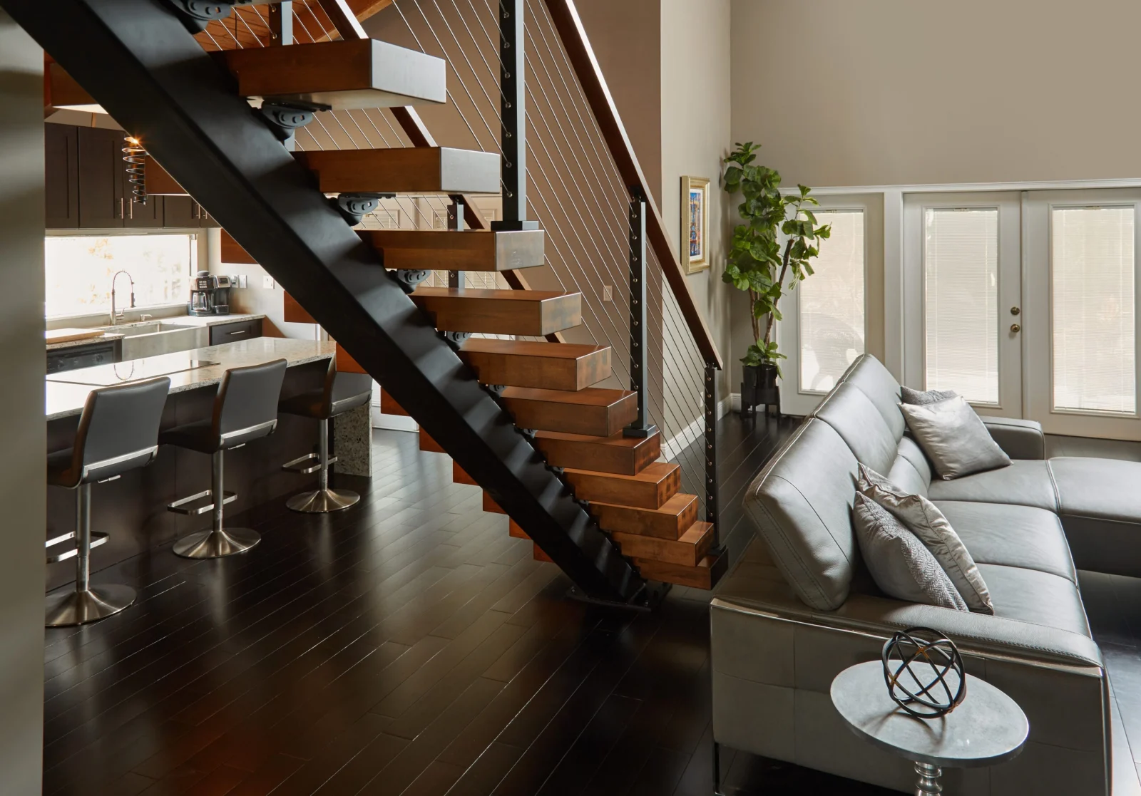 Stair on a black stringer crossing between the kitchen bar and living seating