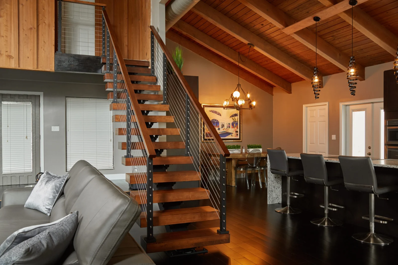 Stair with wood treads beneath a beamed plank ceiling beside a kitchen counter and stools