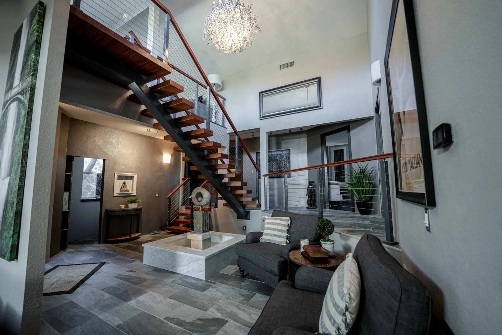 Two-story living room with a stair, reddish handrail and a crystal chandelier above tile
