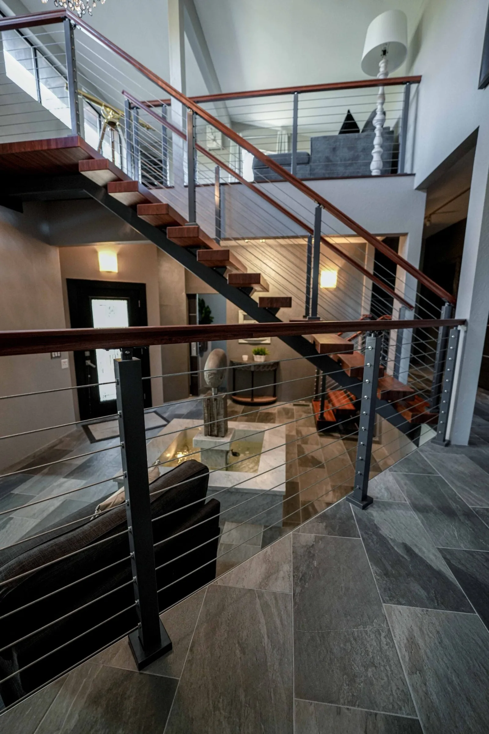 Reddish wood treads and cable railing crossing above a stone-tiled entry