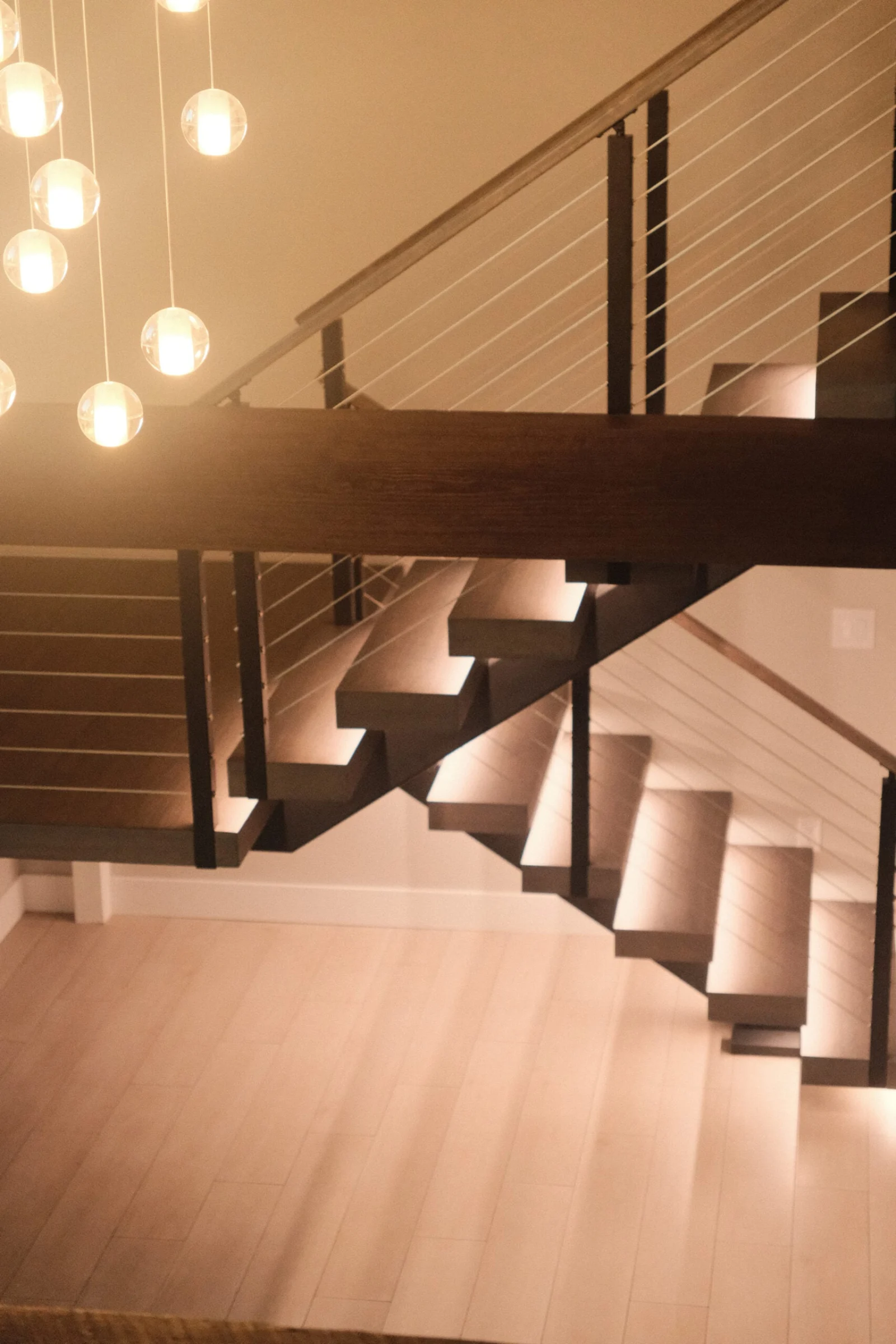 Globe pendants hang beside a dark stair whose underlit treads wash light onto pale floors