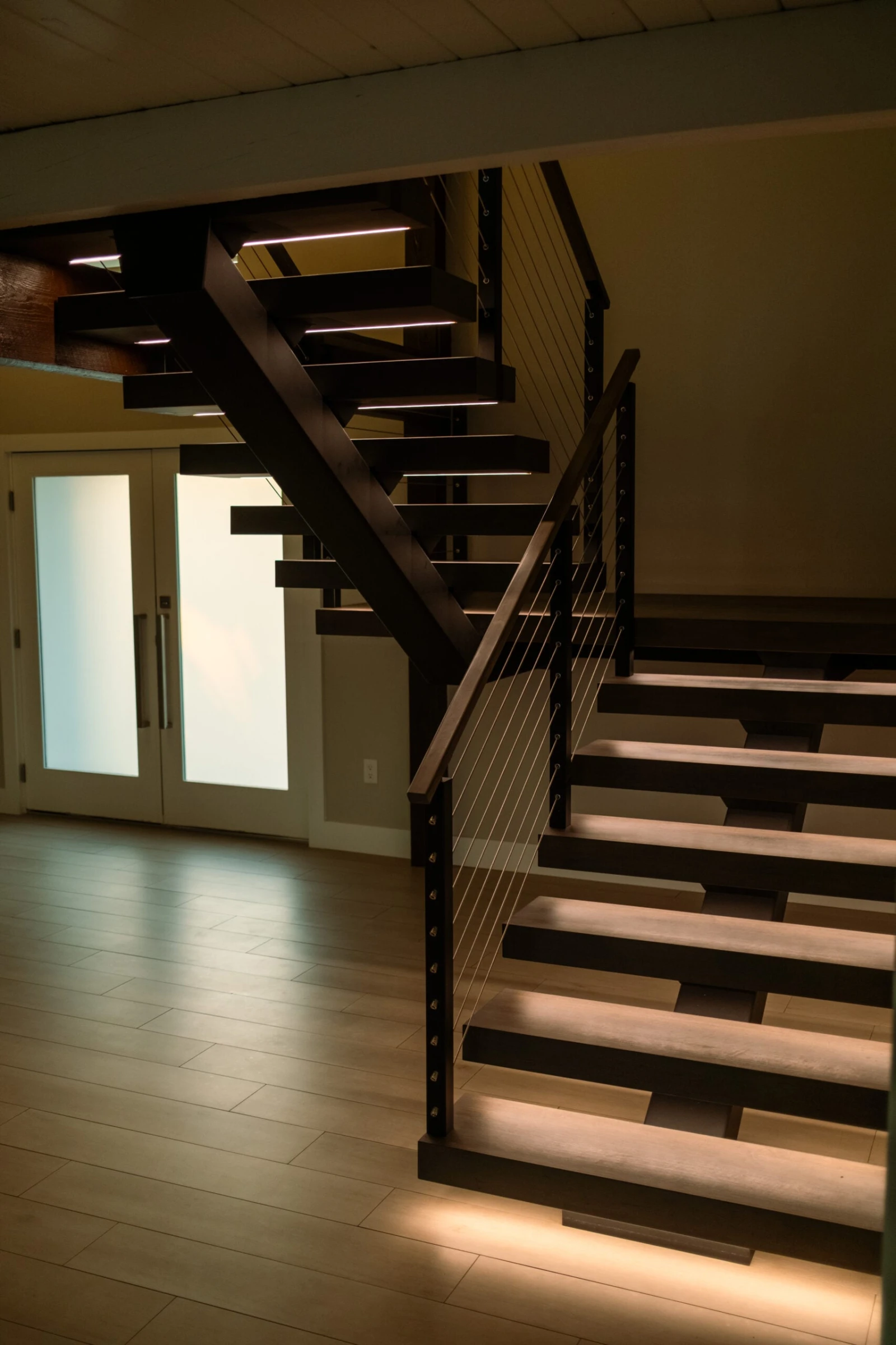 Floating stair with open risers and cable railing rising past frosted glass doors