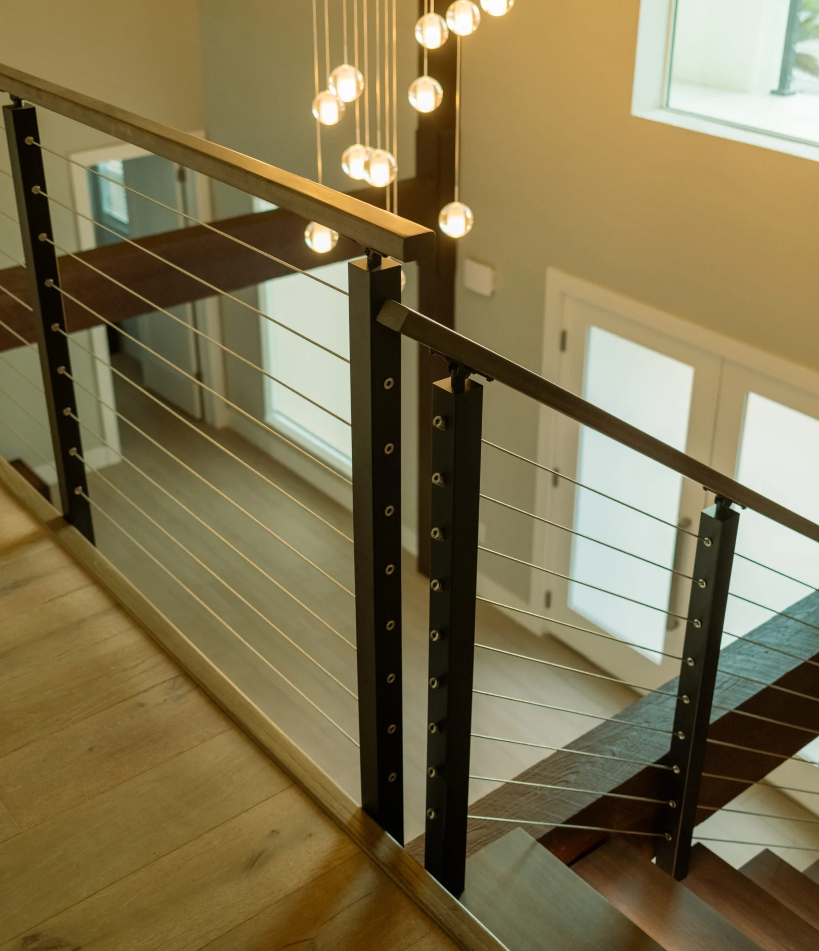 Balcony cable railing with wood top rail beneath a cluster of pendant lights