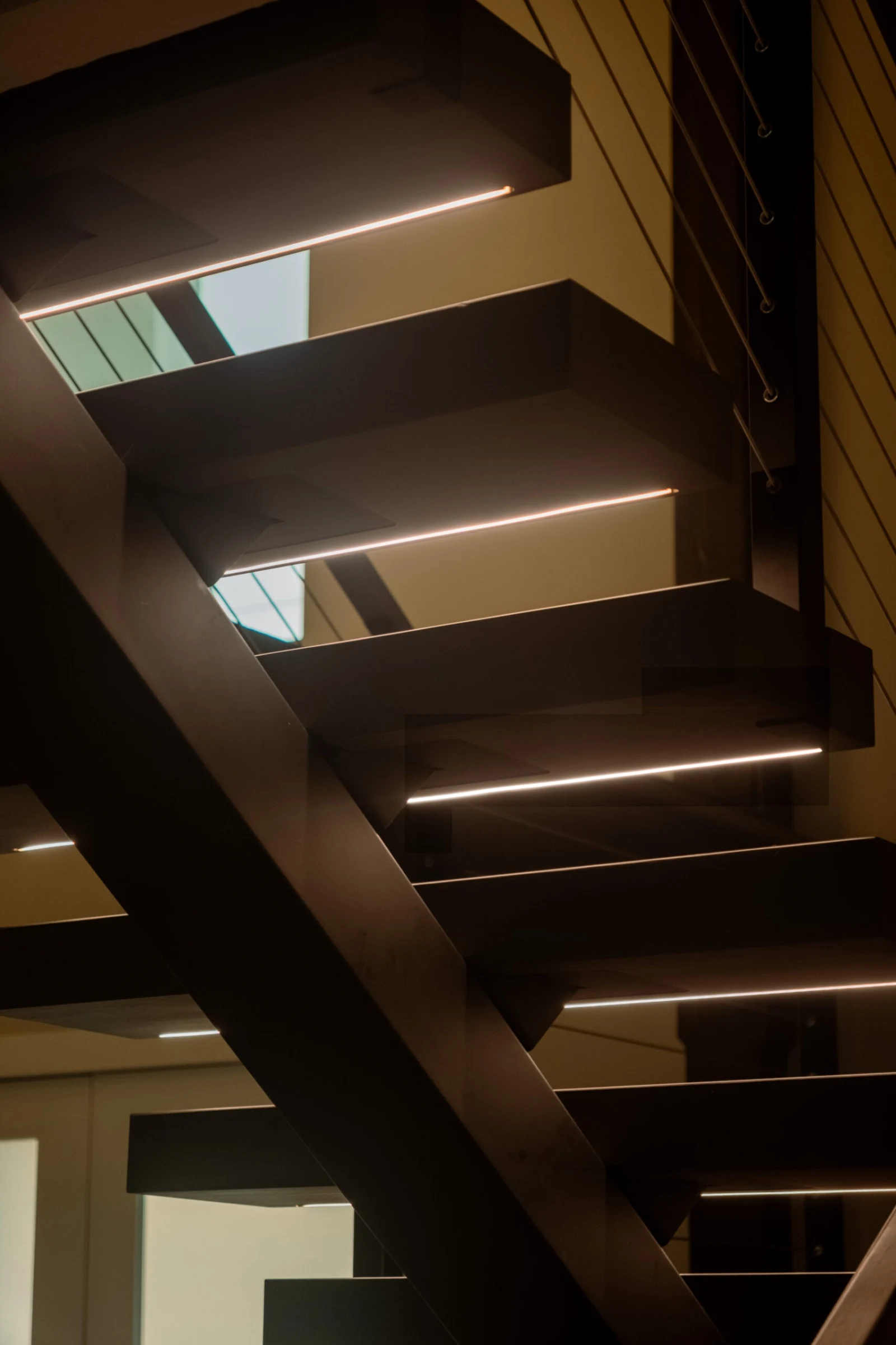Looking up at glowing tread edges beneath a dark floating stair
