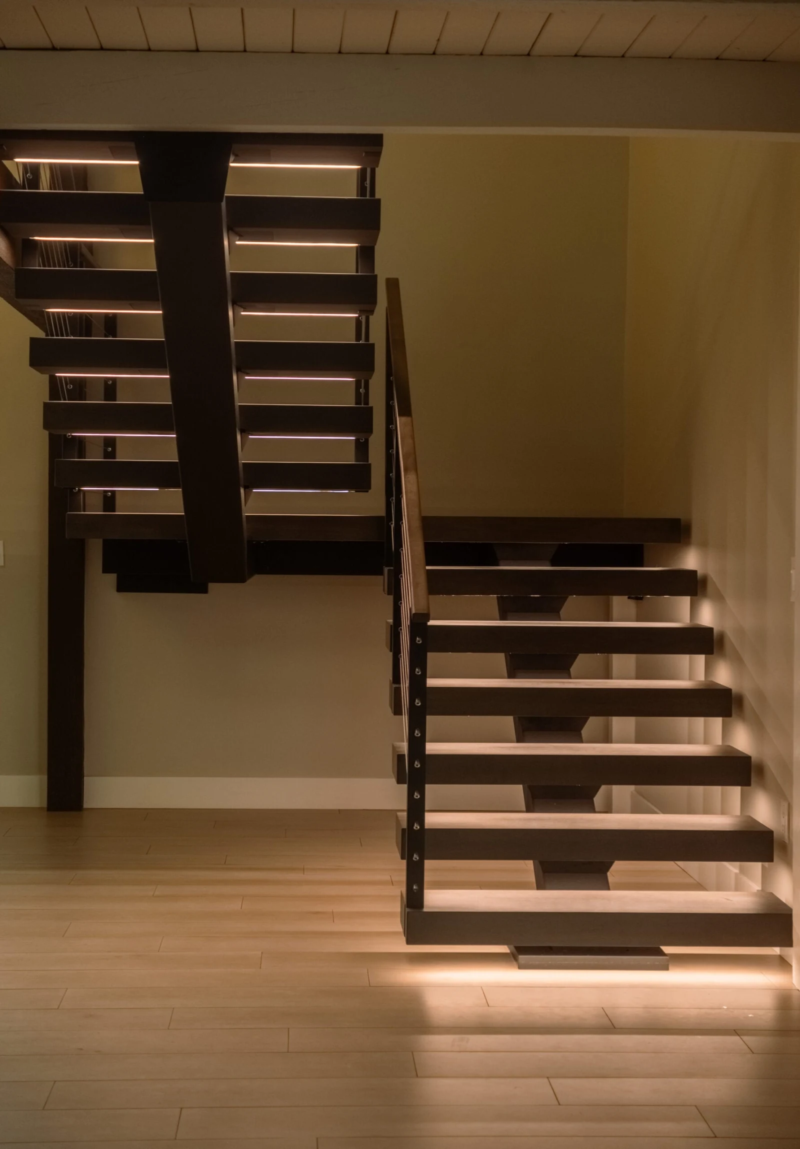 Two floating stair flights meet across a room with light wood flooring