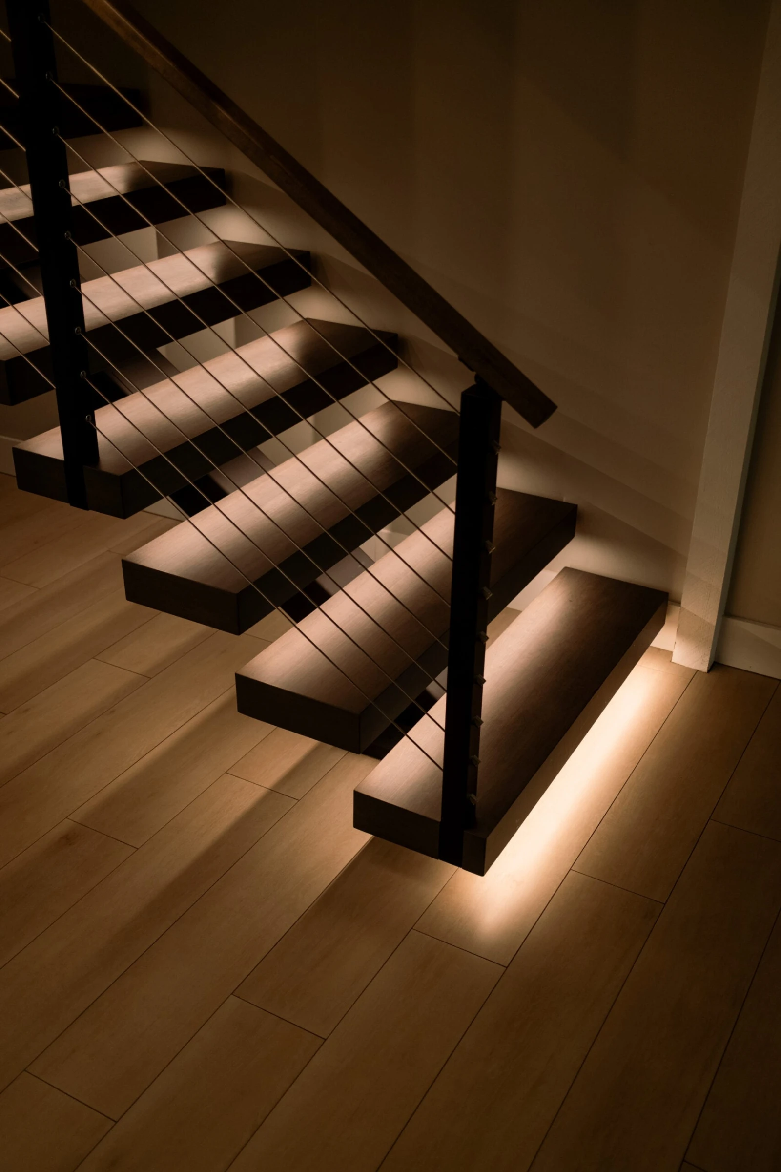 Bottom treads glowing with under-tread lighting above wide-plank wood flooring