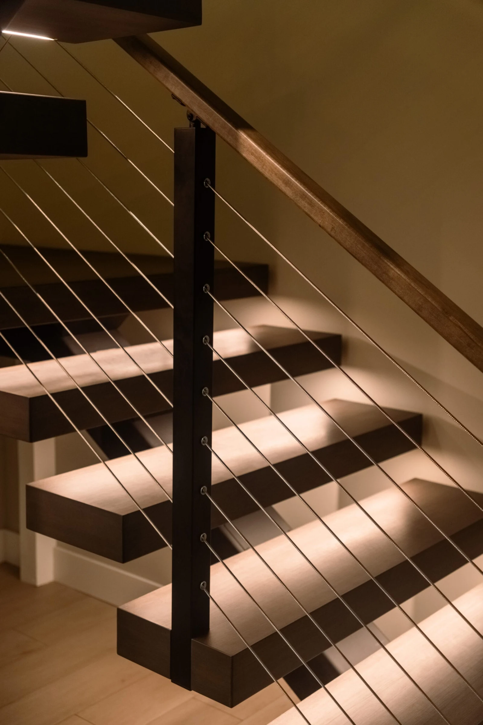 LED-lit dark wood treads and cable railing beside a slim black post