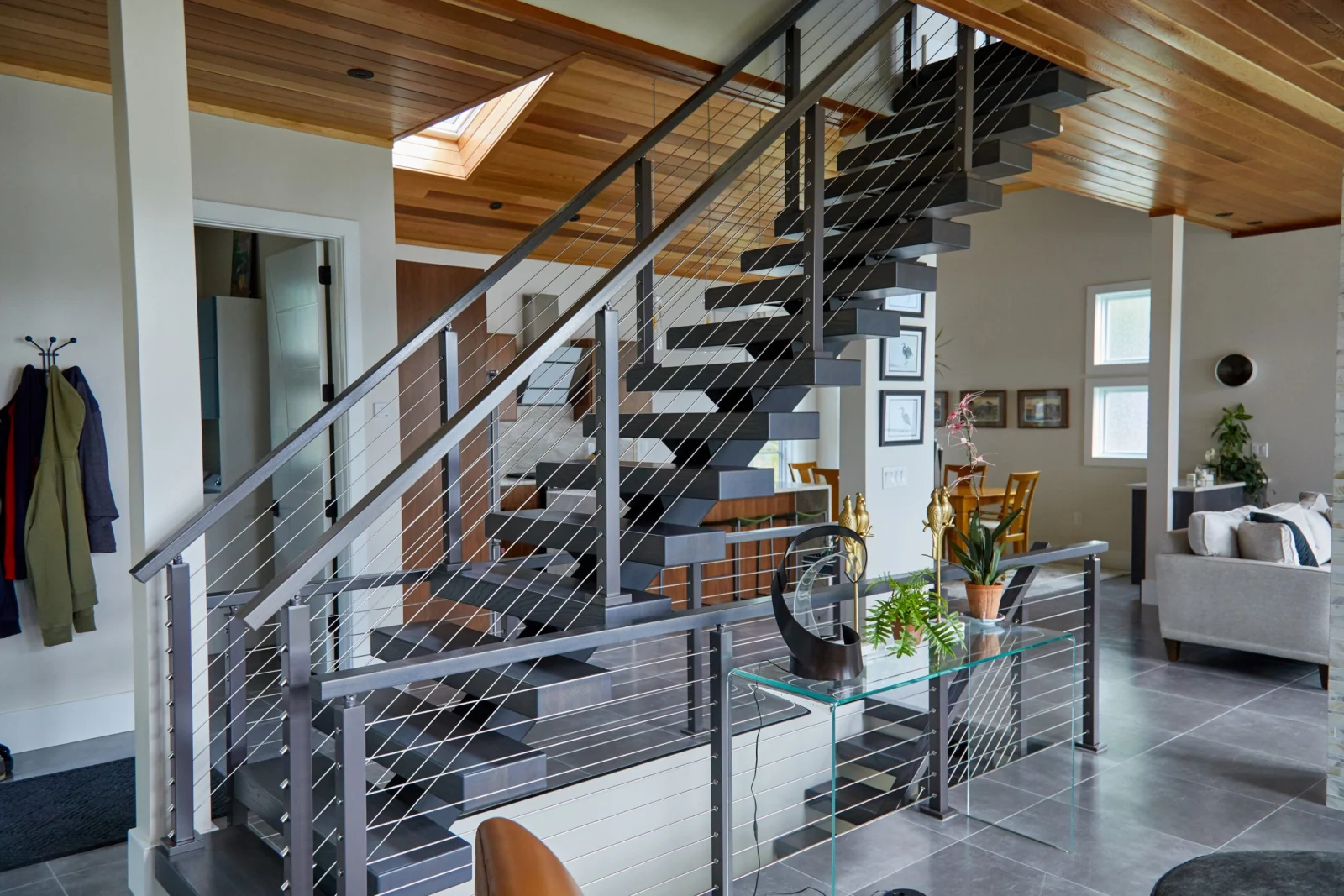 Gray treads and cable railing under a warm plank ceiling with a skylight above