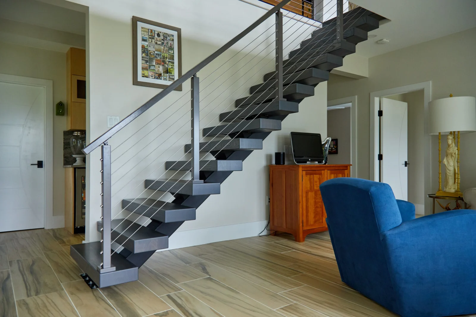 Gray floating stair with cable railing climbing a living room wall