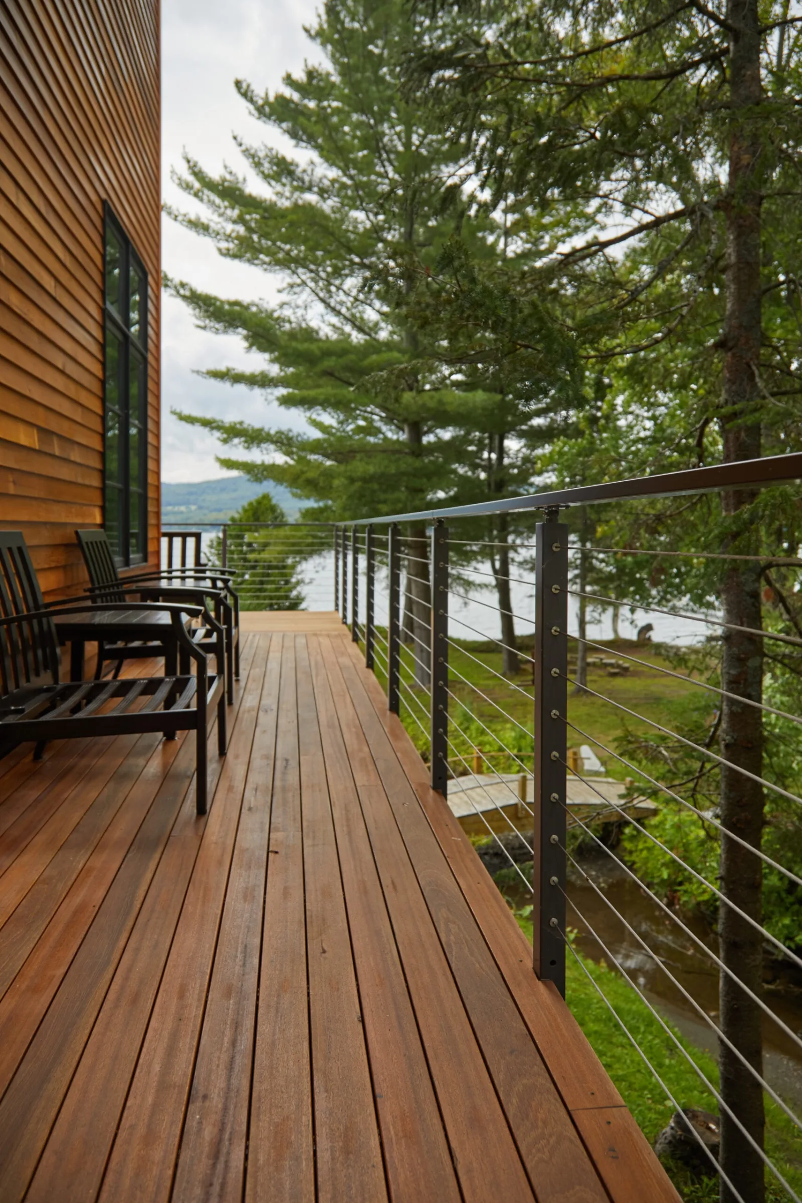 Deck cable railing along a covered porch overlooking a lake and evergreens