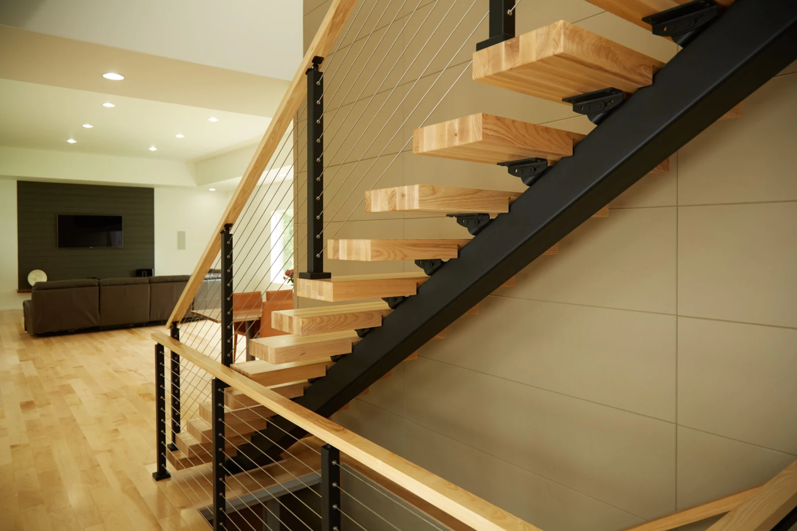 Thick light treads on a black stringer beside a large-format tile wall in a lower level