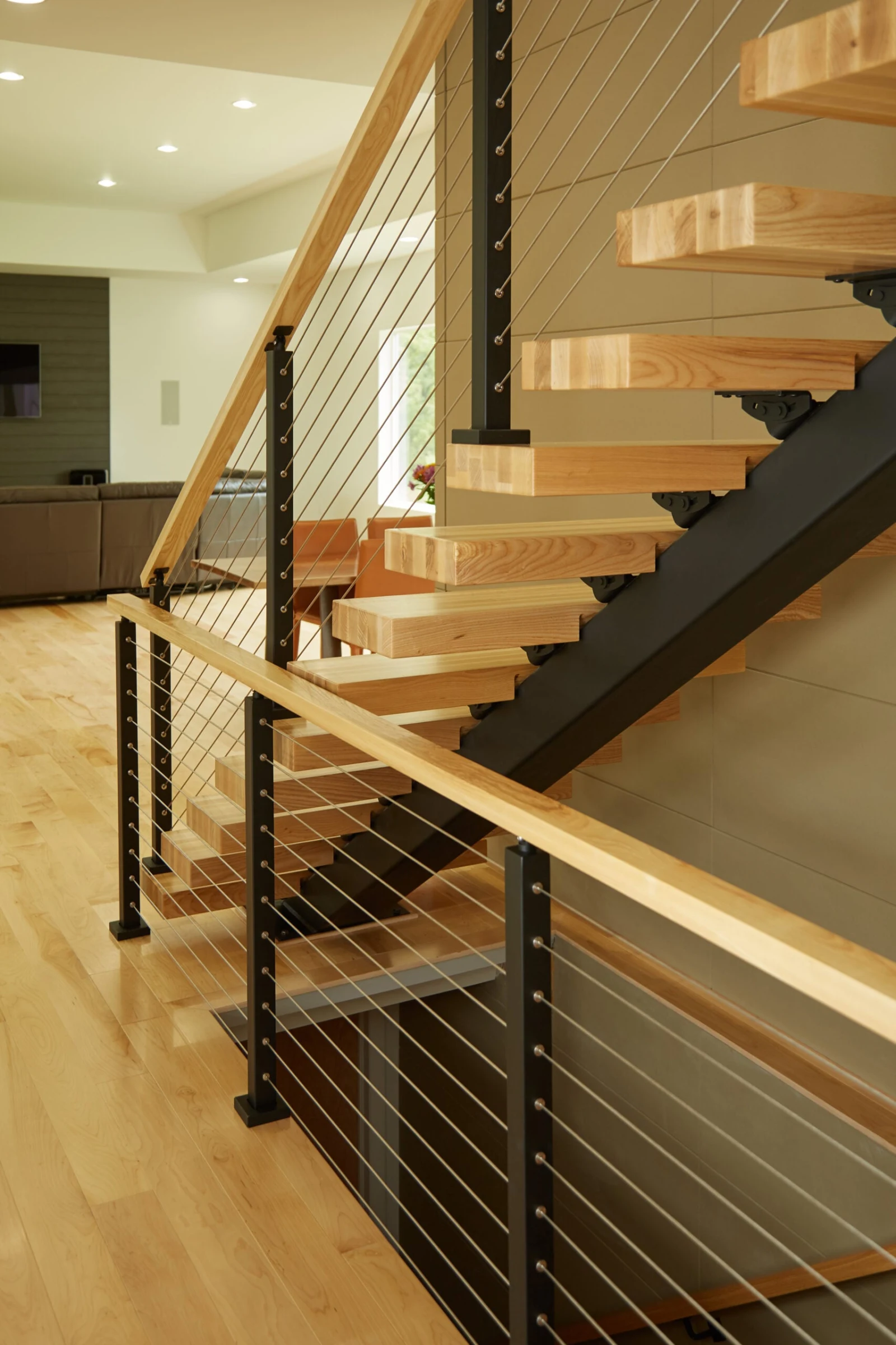Light wood treads on a black stringer with cable railing and wood top rail