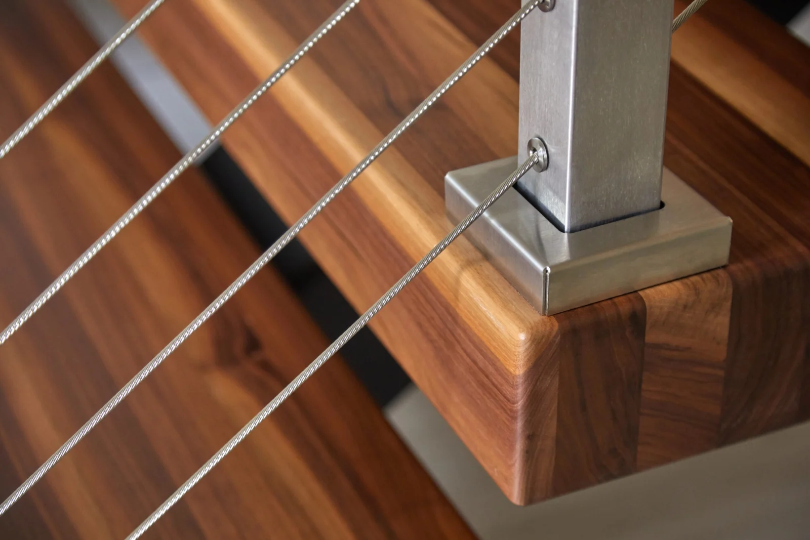 Base of a stainless post clamped to a wood tread with angled cables