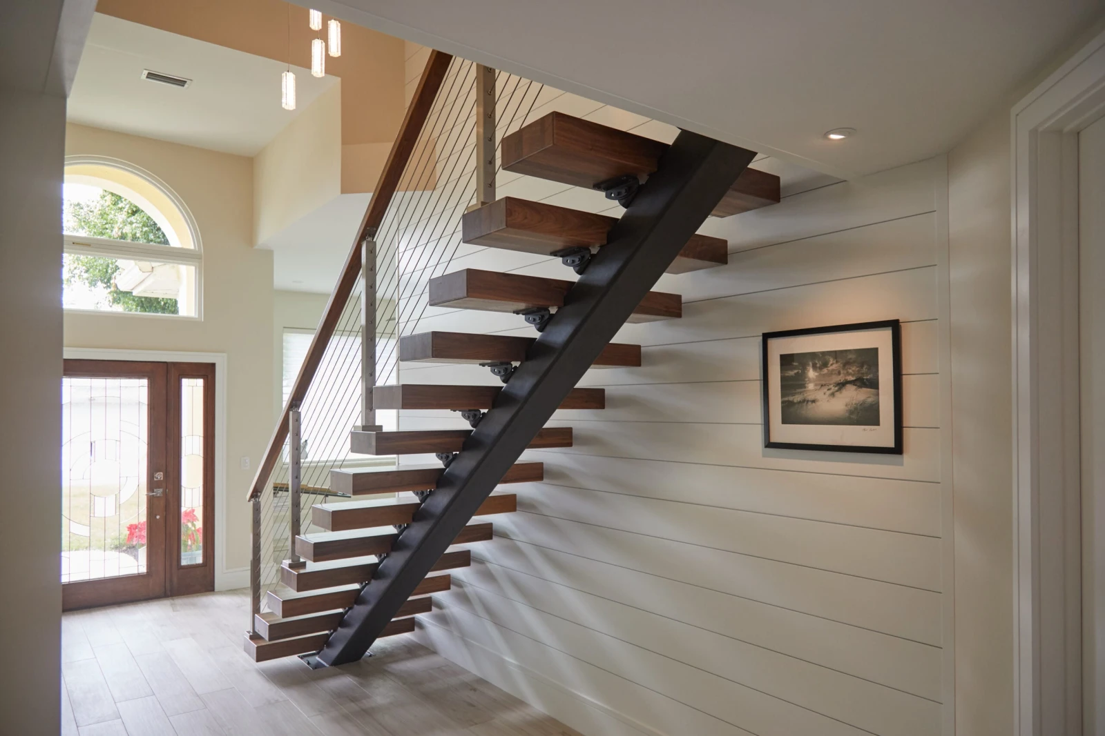 Dark treads against a white shiplap wall in an entry with an arched transom window