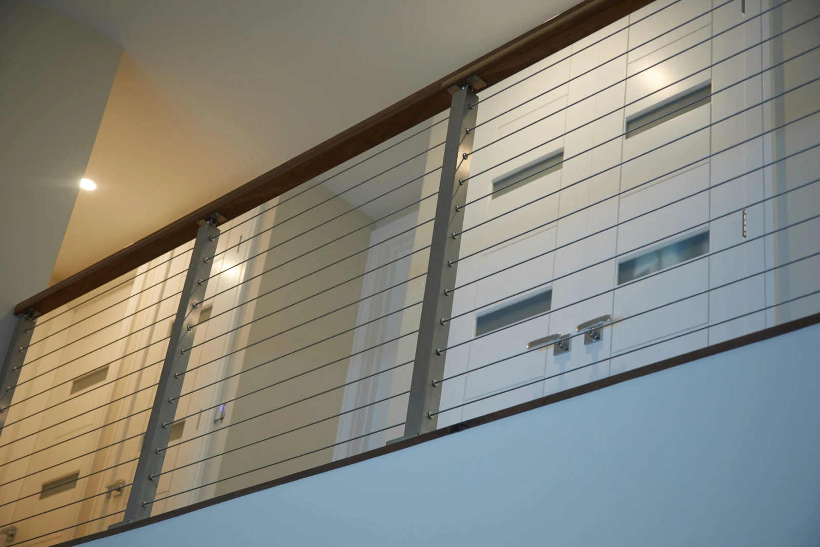 Stainless posts and cable infill along a balcony above white shiplap walls