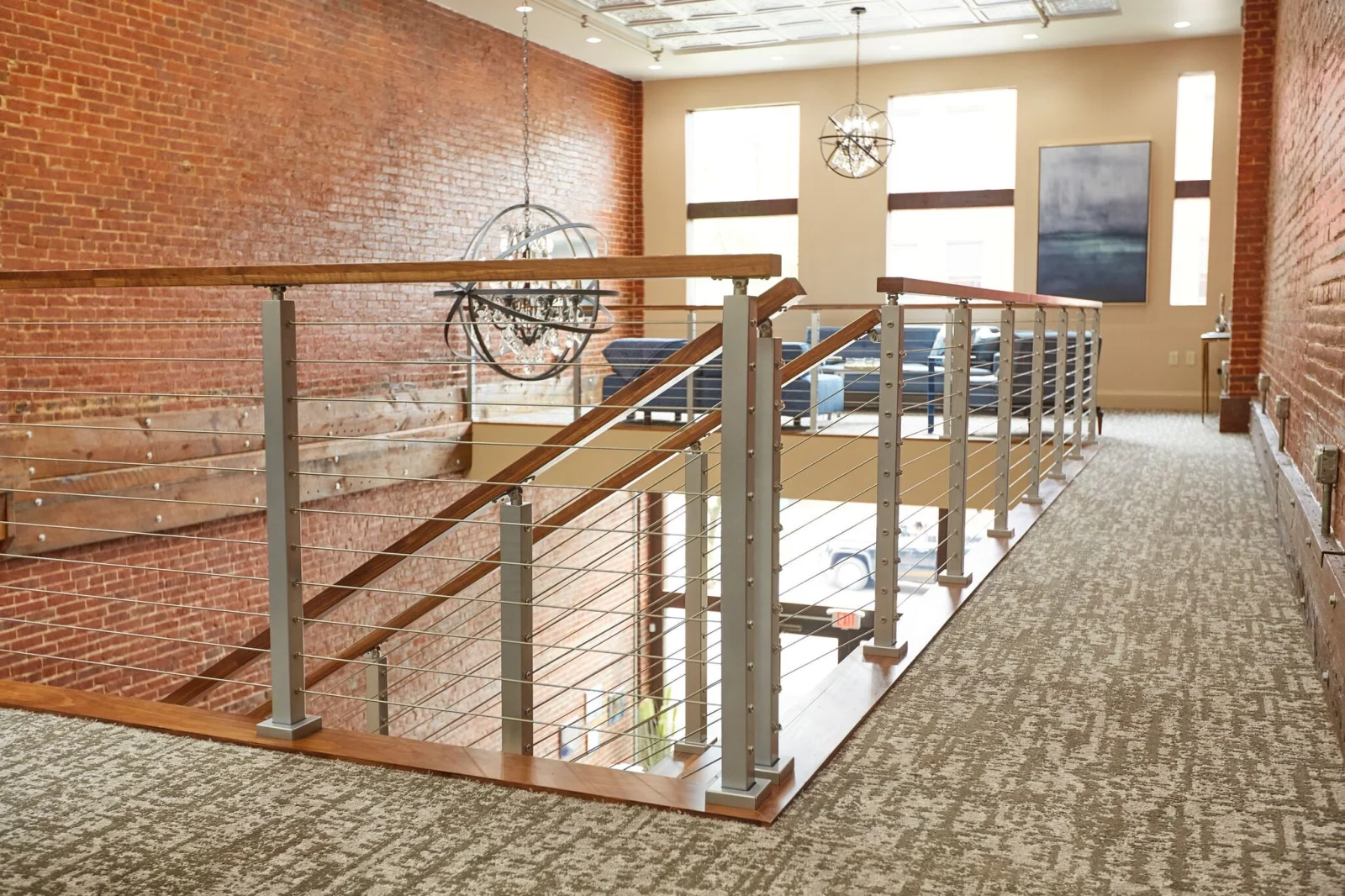 Cable railing wrapping a carpeted loft overlook inside a brick-walled office