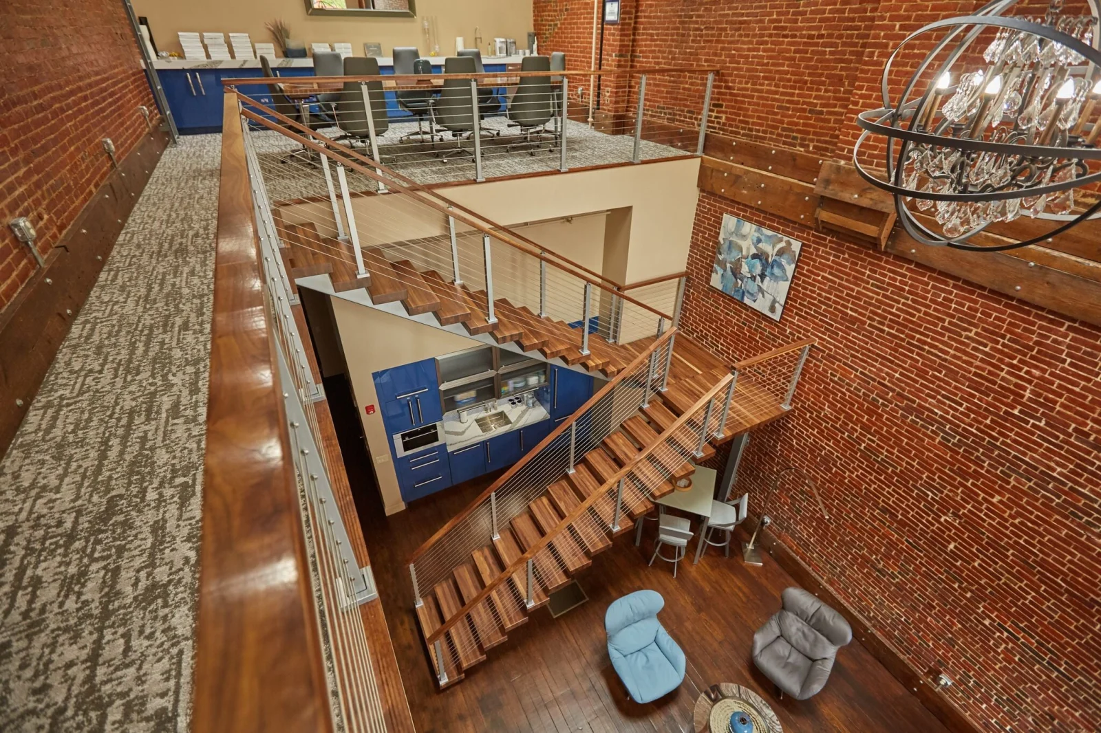 Looking down from a mezzanine over brick walls, cable railing and an orb chandelier