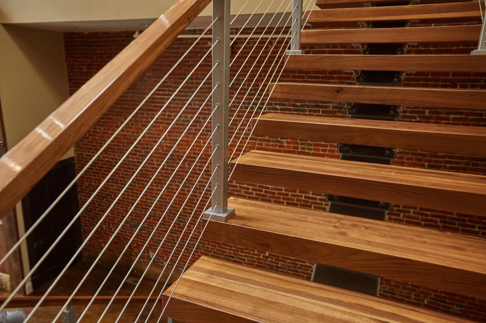 Looking down wood treads with cable railing against an exposed brick wall