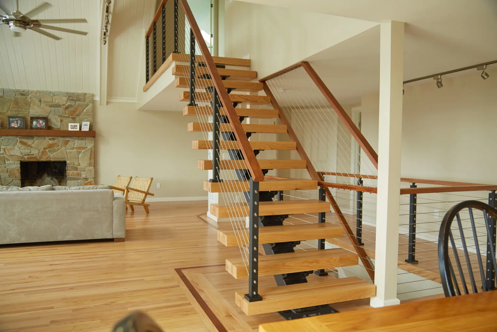 Floating stair rising beside a stone fireplace in an open living room
