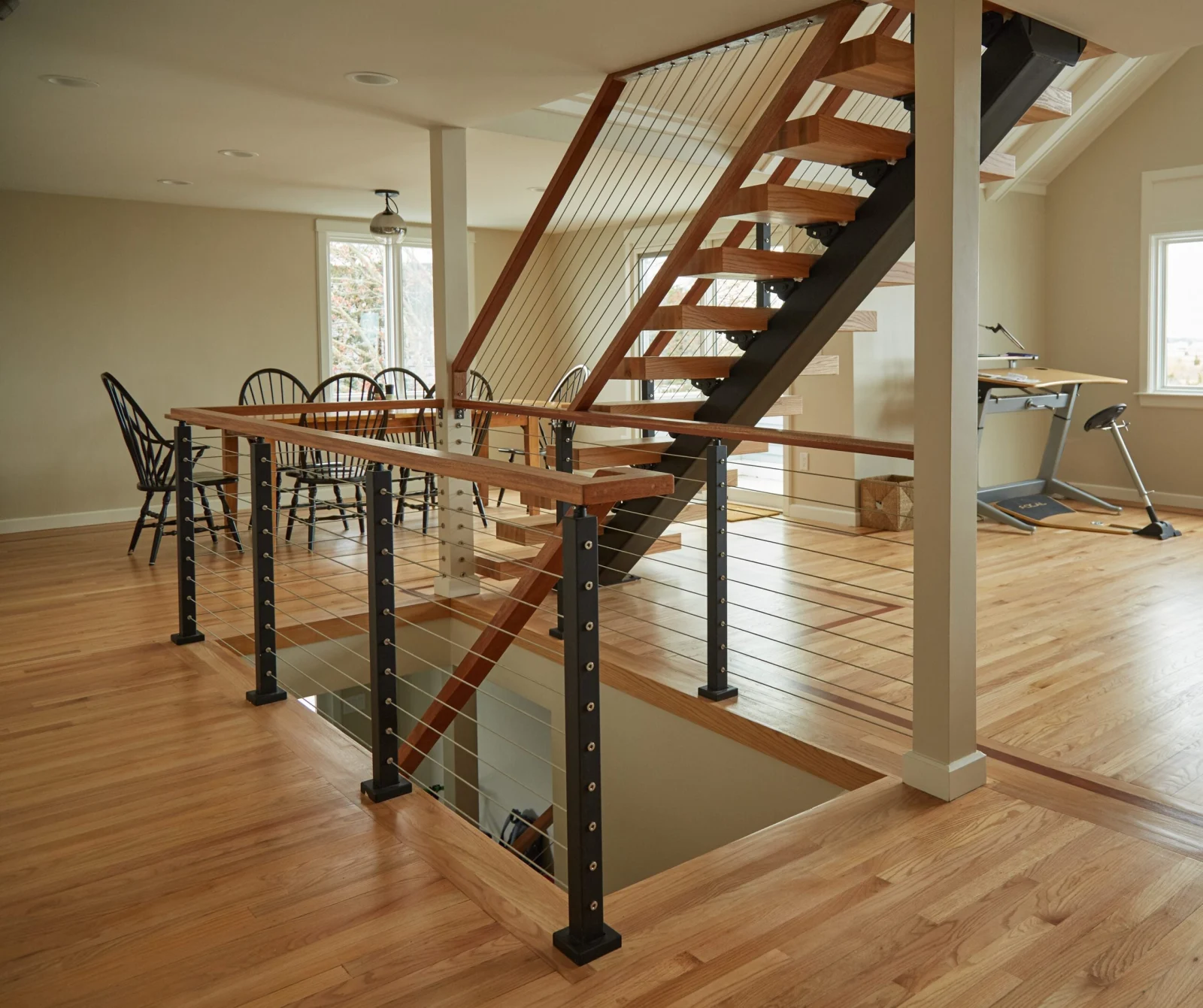 Stair and balcony cable railing seen across a dining area and wood floor