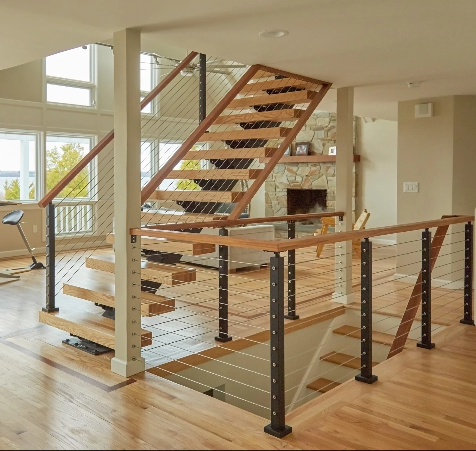 Cable railing wraps a landing in a great room with a stone fireplace beyond