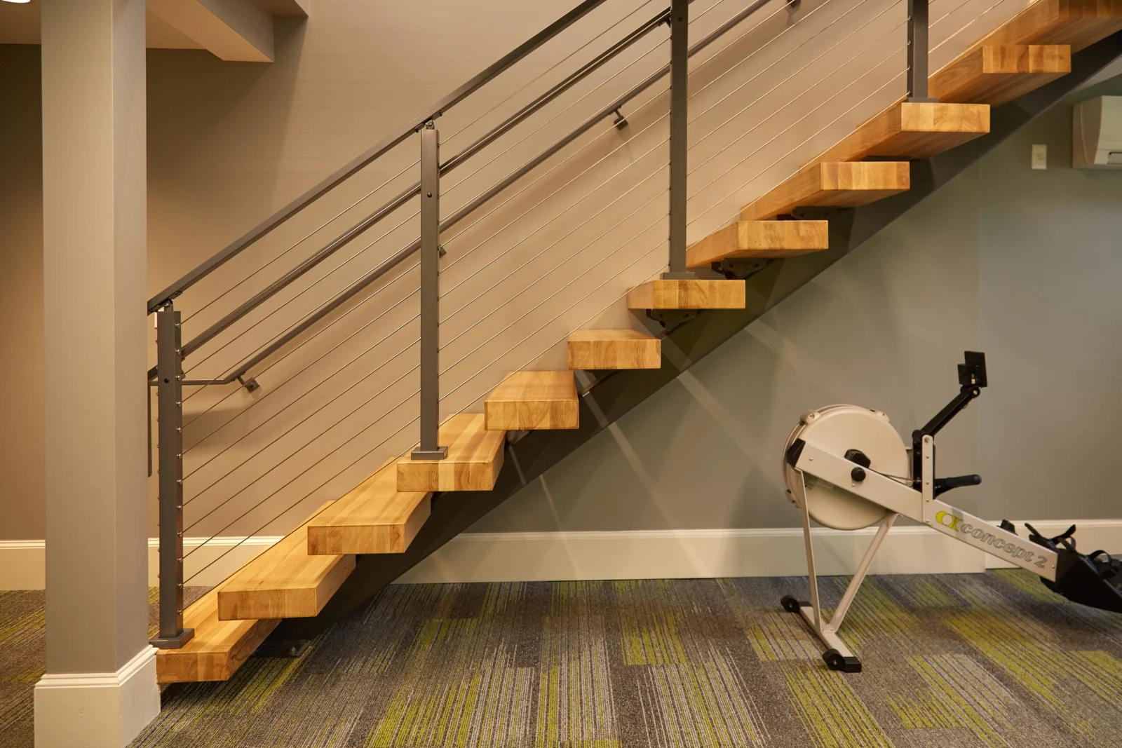 Straight flight of wood treads with cable railing above patterned carpet tile