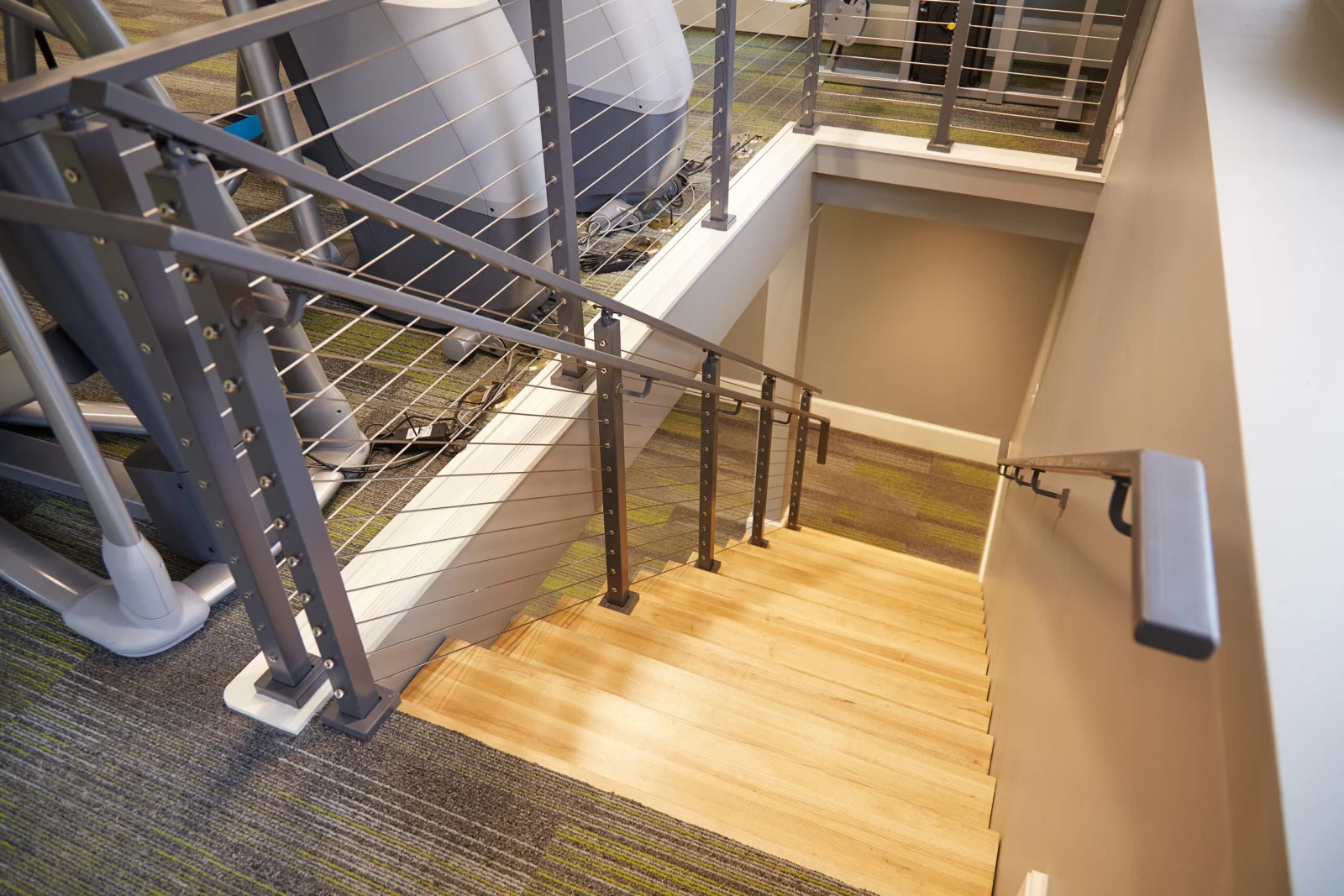 Looking down a wood stair into a gym with cable railing overlooking equipment