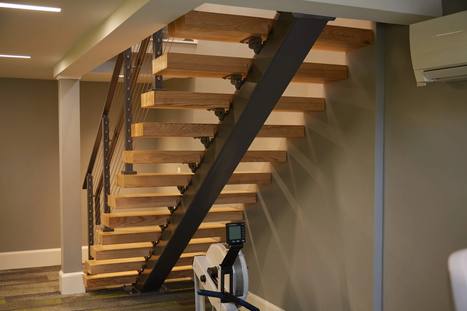 Floating stair with dark stringer seen across a lower-level workout area