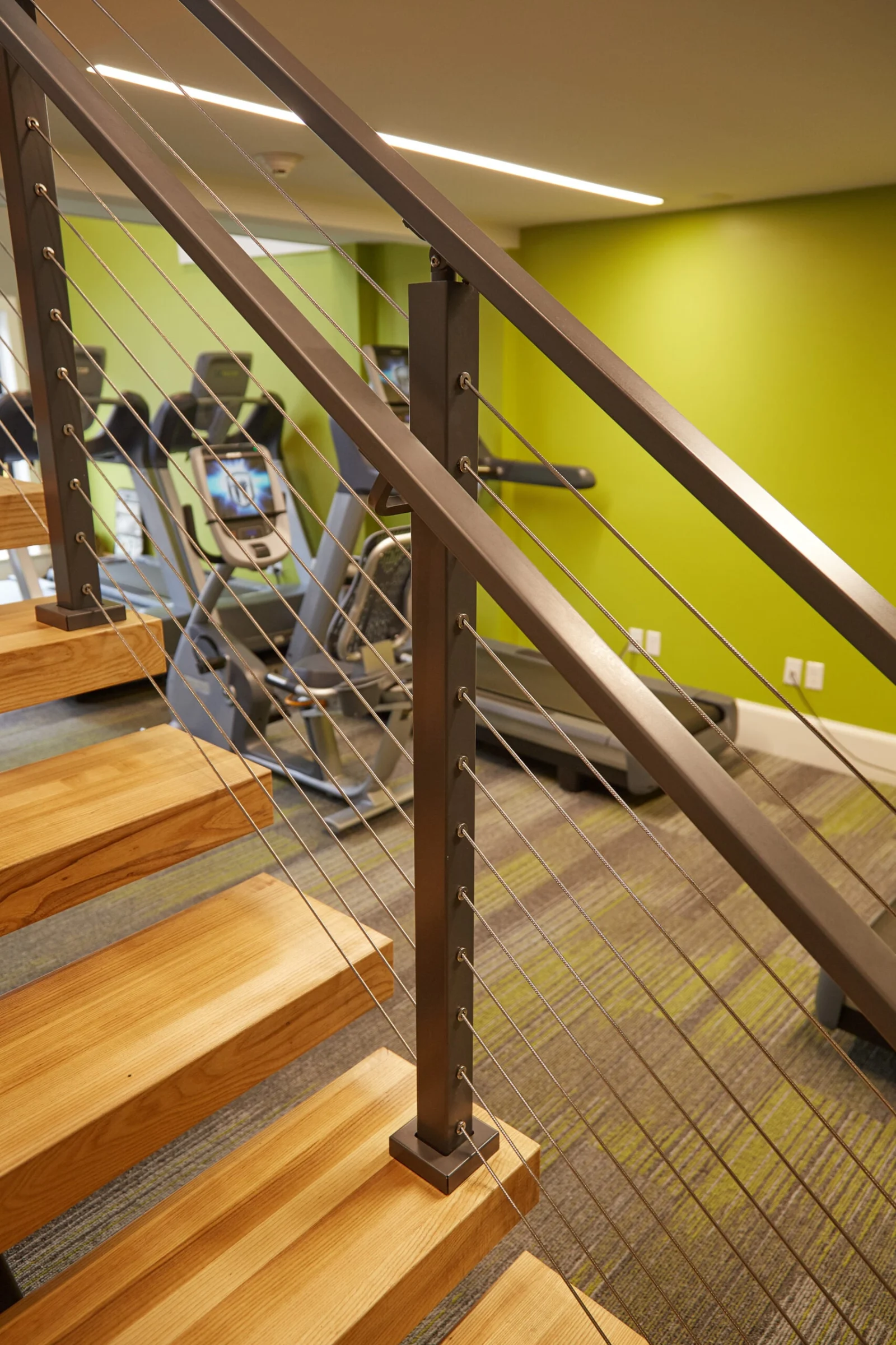 Bronze-toned posts and cable railing beside treads with a green gym wall