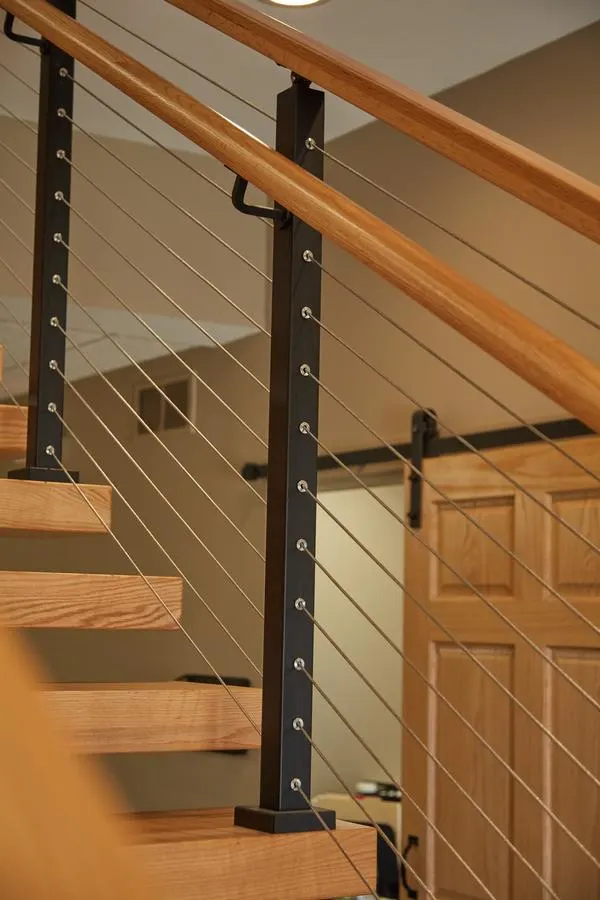 Black posts and cable infill beside a wood handrail and open treads