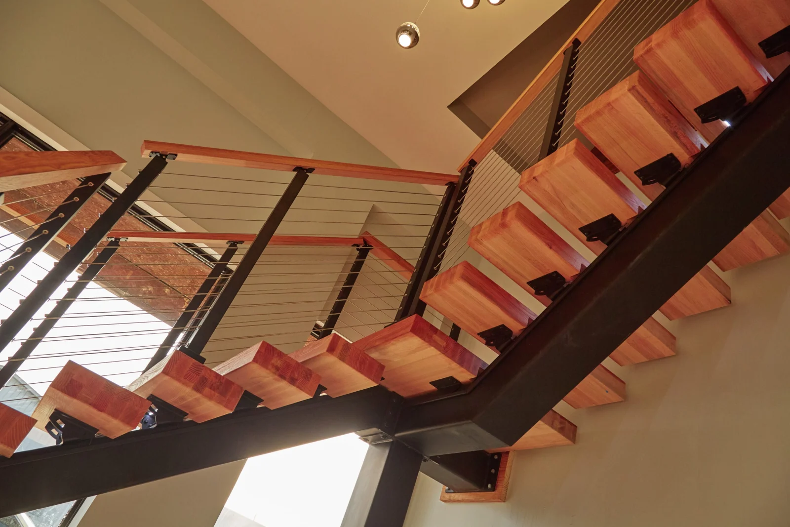 Seen from below, reddish treads cantilever off a dark stringer between two crossing flights