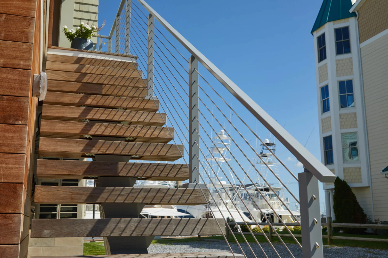Wood treads cantilever above gravel while white rods angle down toward a boat marina