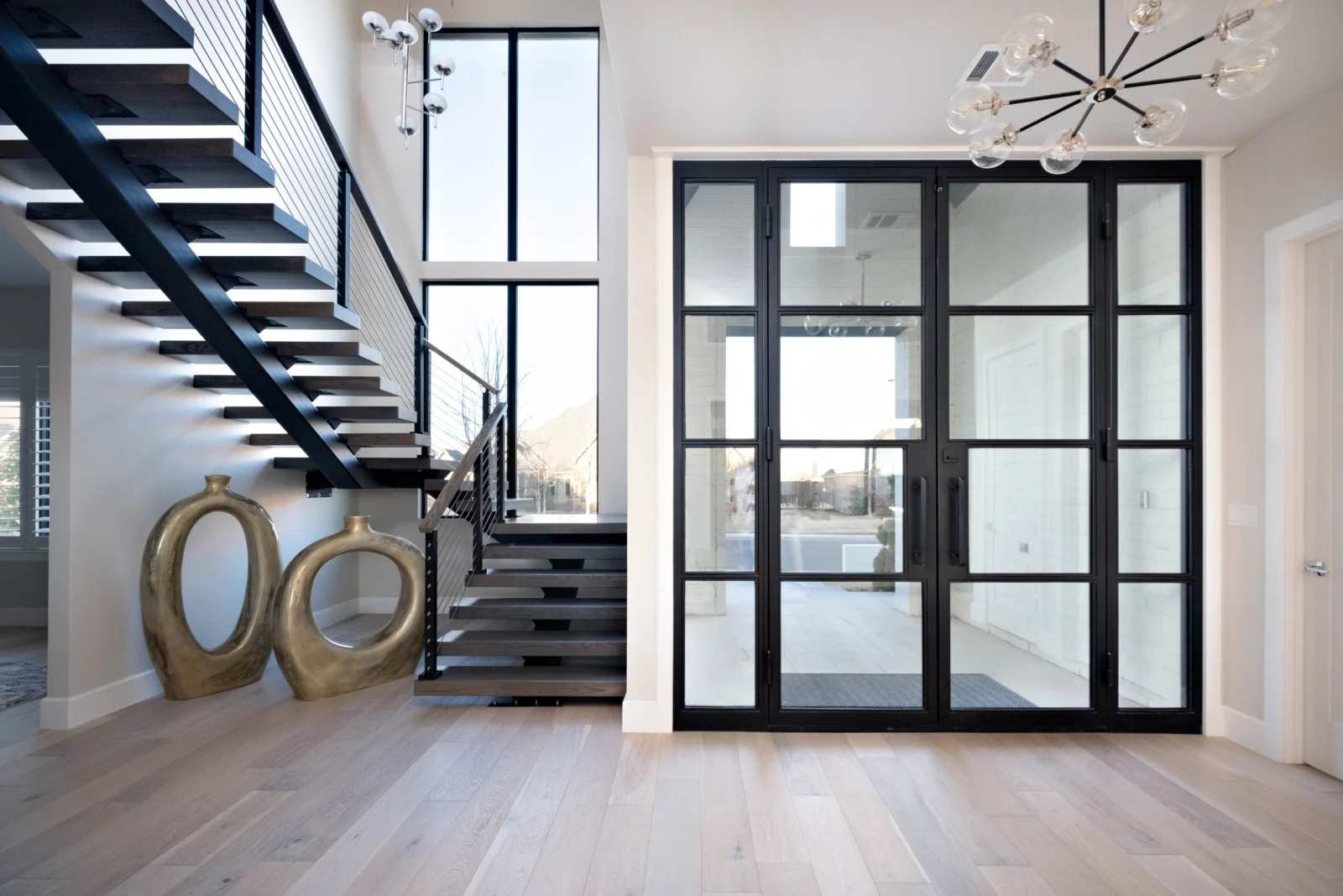 Wide entry with the stair at left and black-framed glass doors opposite