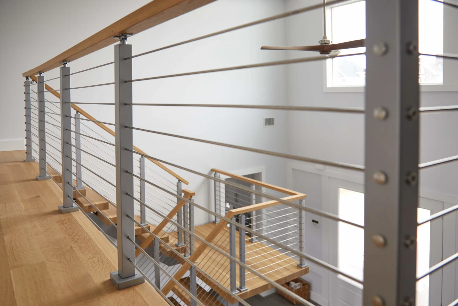 Balcony rod railing running past a double-height wall with a ceiling fan beyond