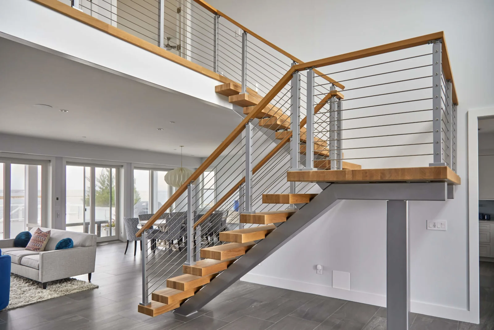 Switchback floating stair with brushed silver stringer, rod infill and a wood top rail