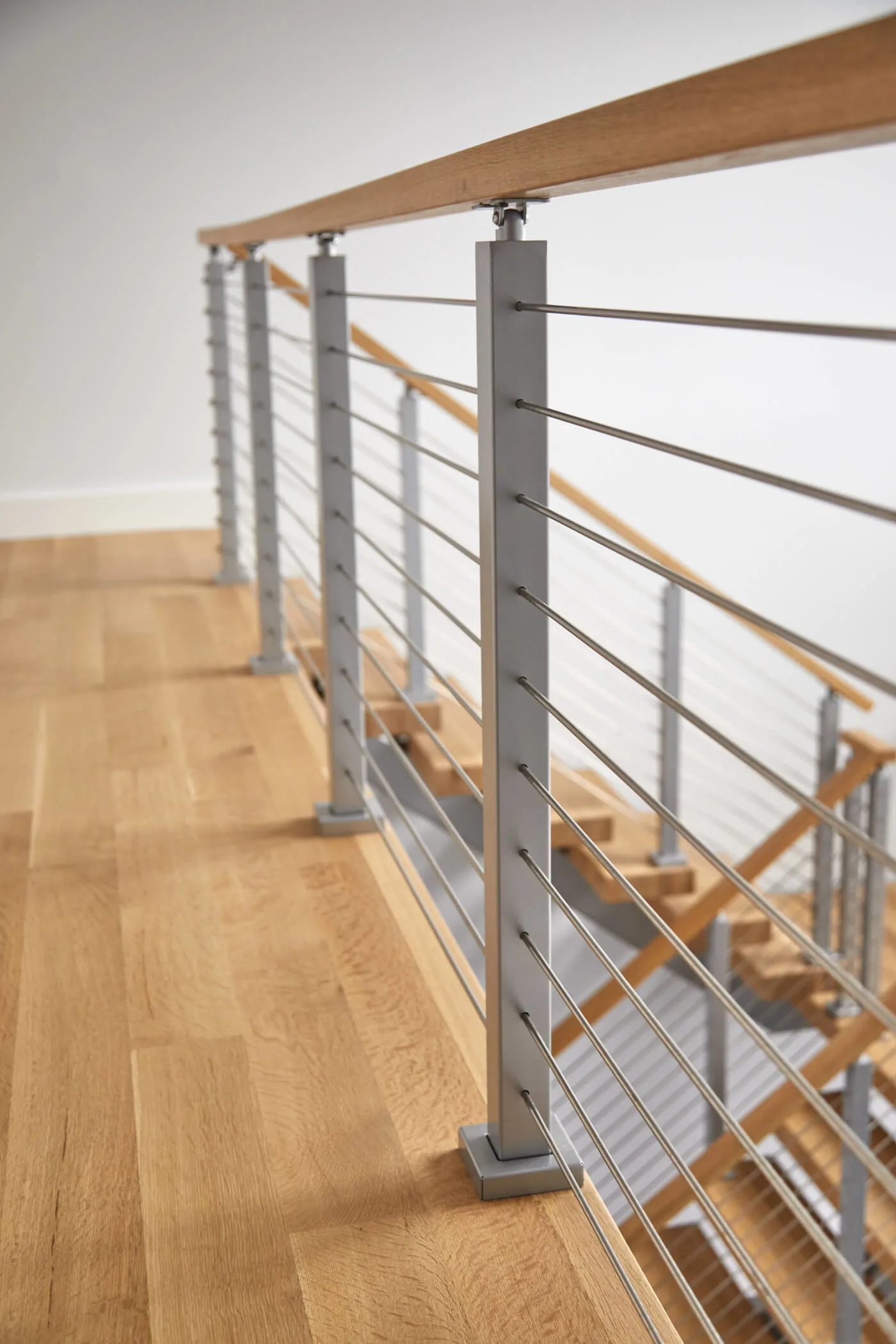 Angled view along the gray posts and rods above wide-plank flooring