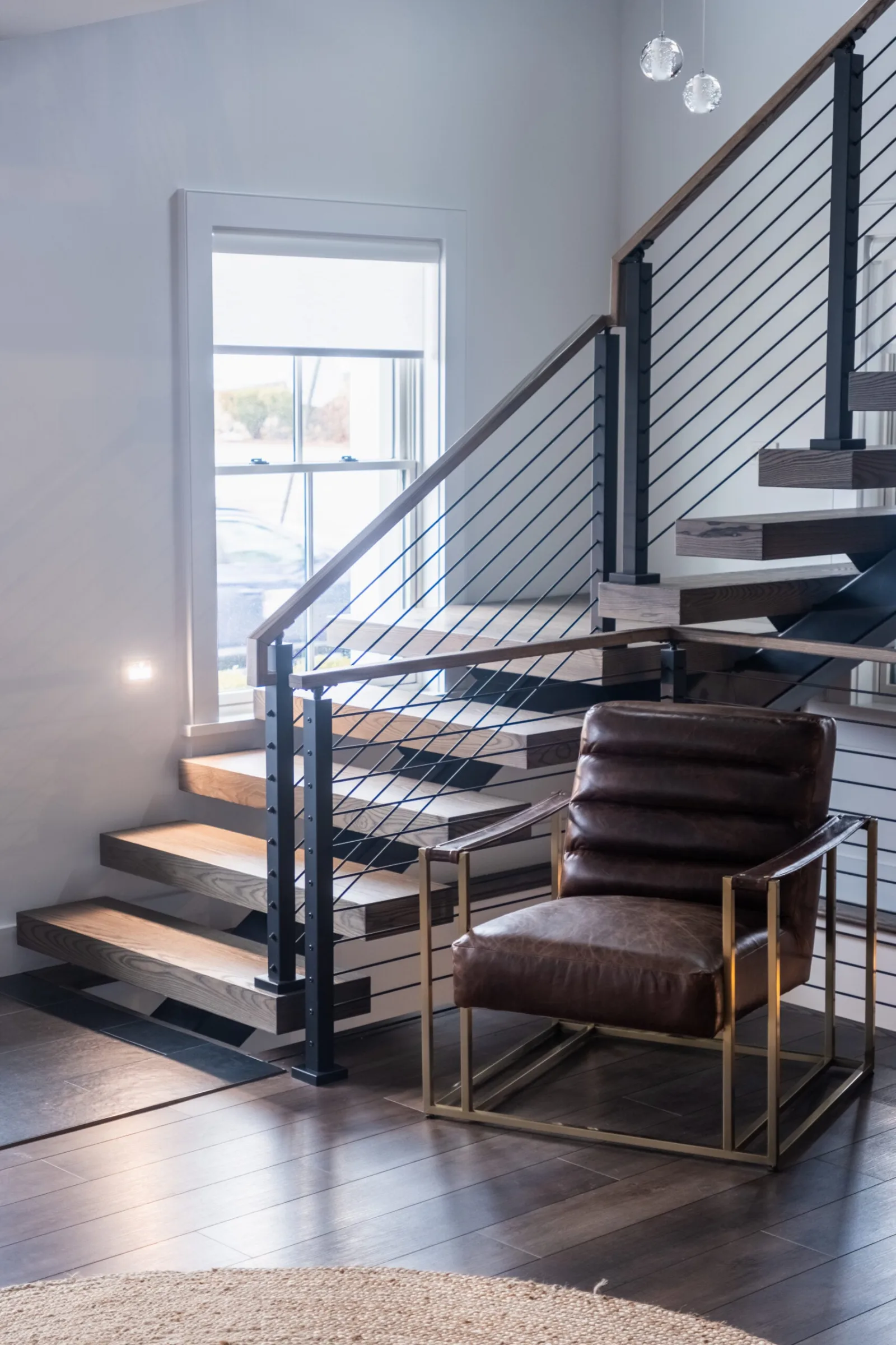 Stair beside a tall window with a leather chair on dark wood flooring