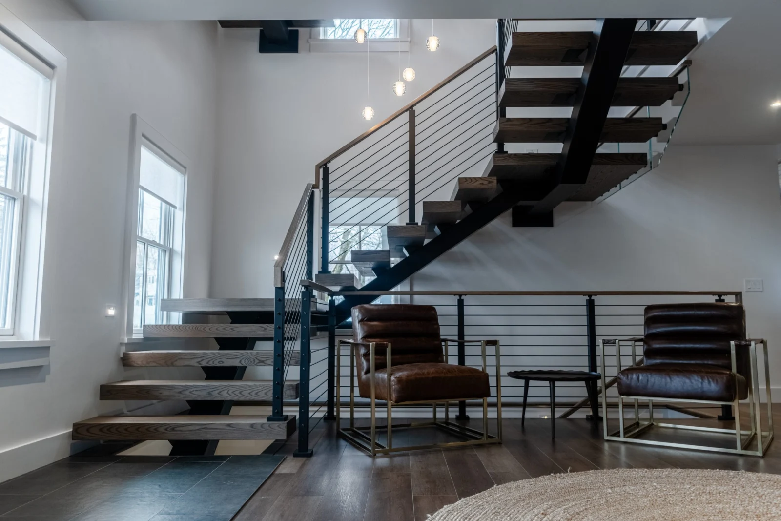 Floating stair on a black center stringer with rod railing above leather chairs