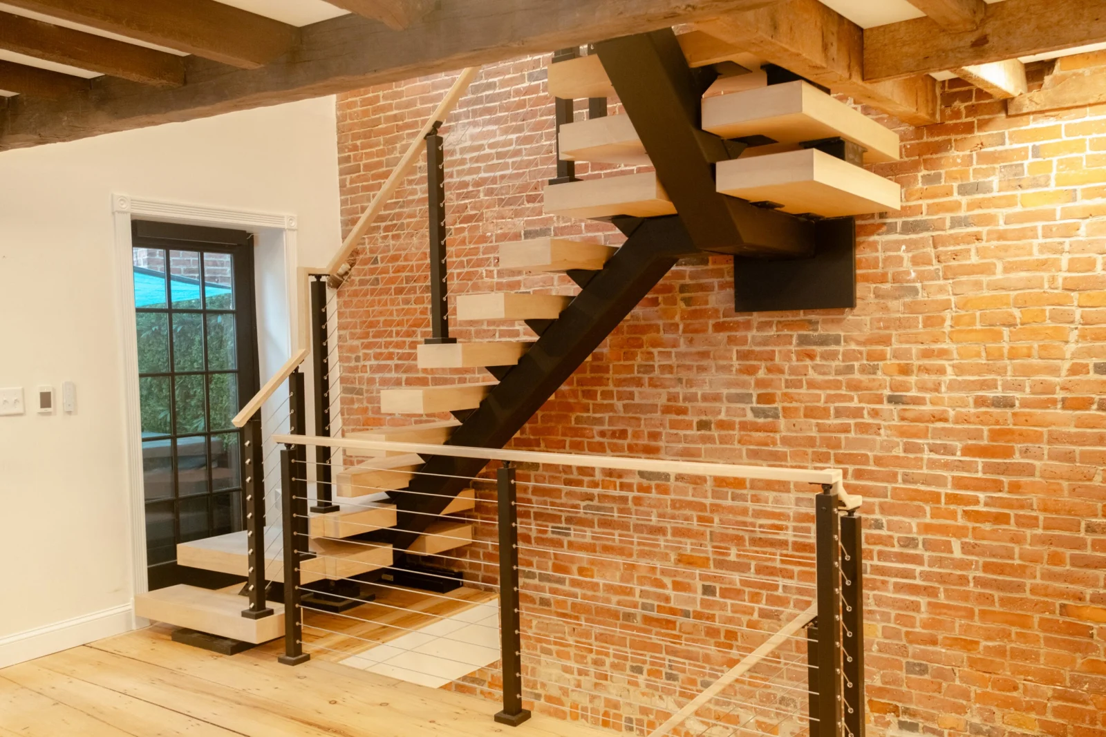 Pale treads on a black stringer set against an old brick wall and timber beams