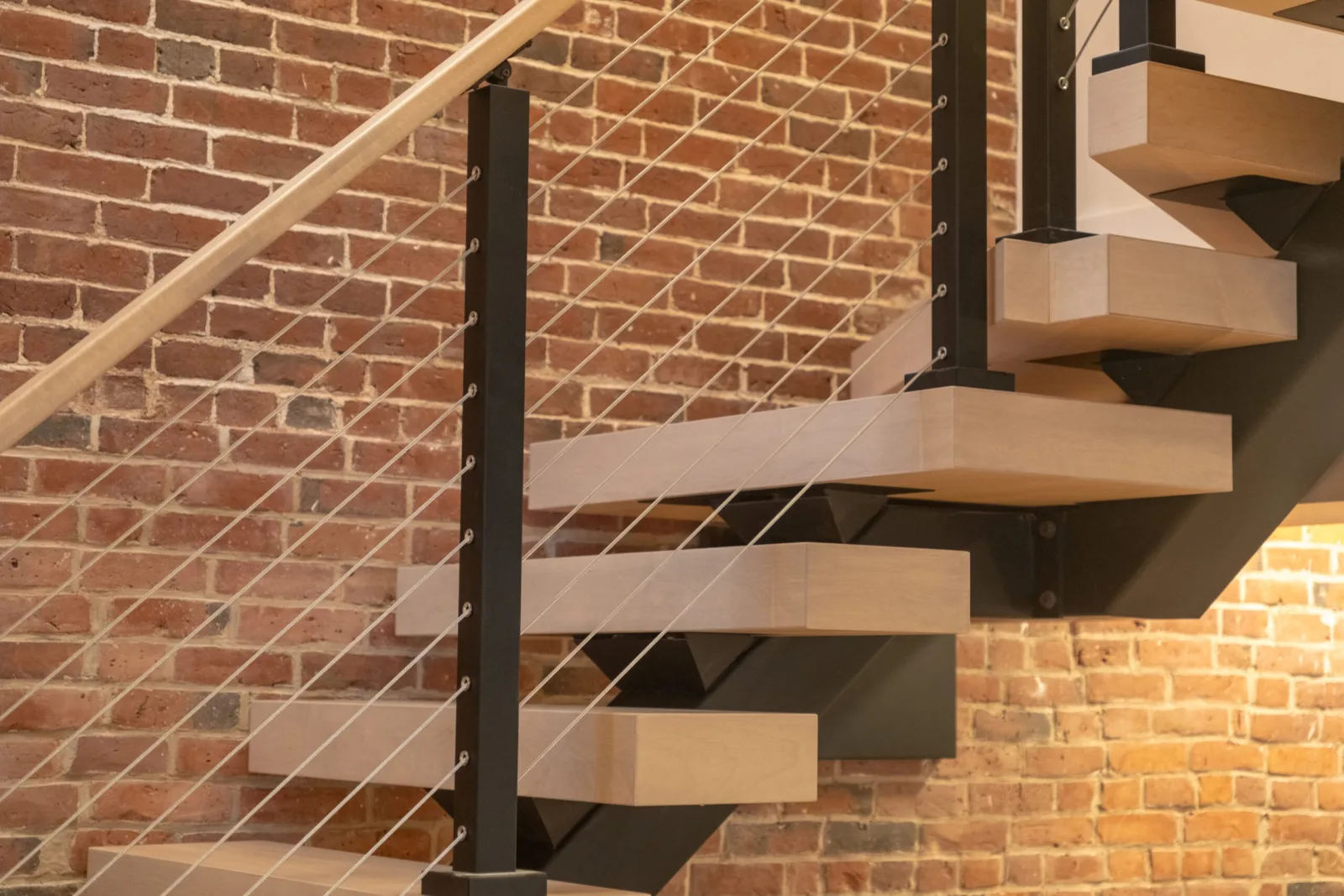 Cantilevered treads off a black stringer in front of old brickwork
